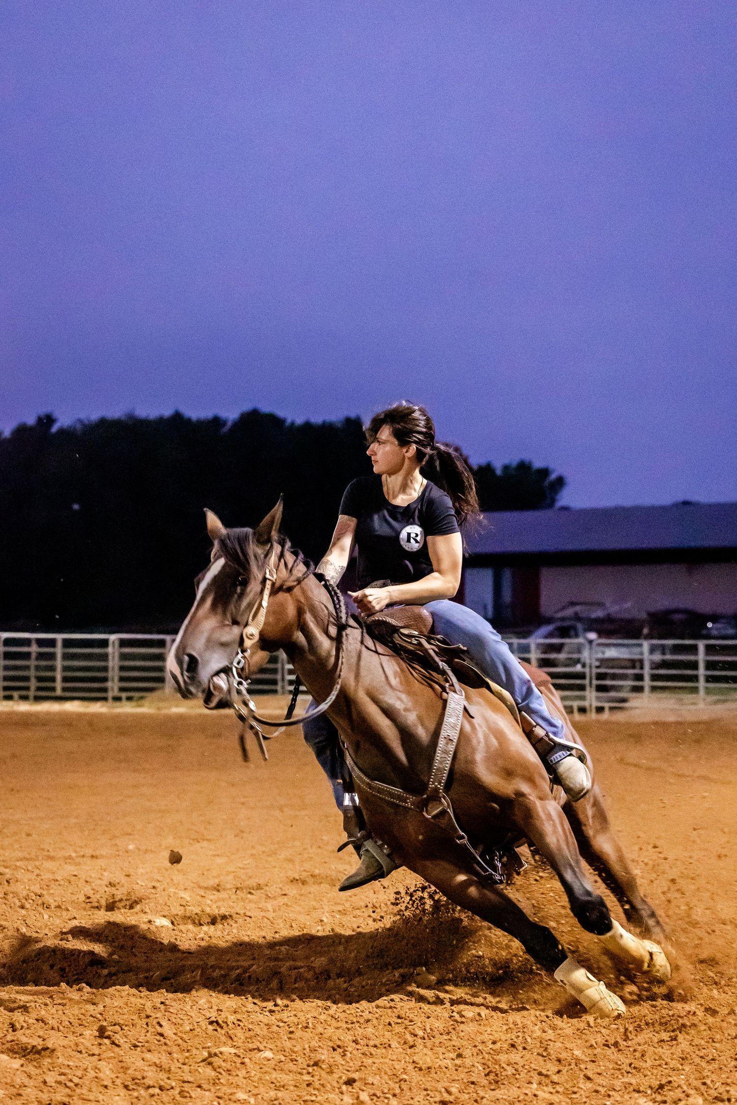 Horse and rider executing a sharp turn in a dirt arena during evening practice.