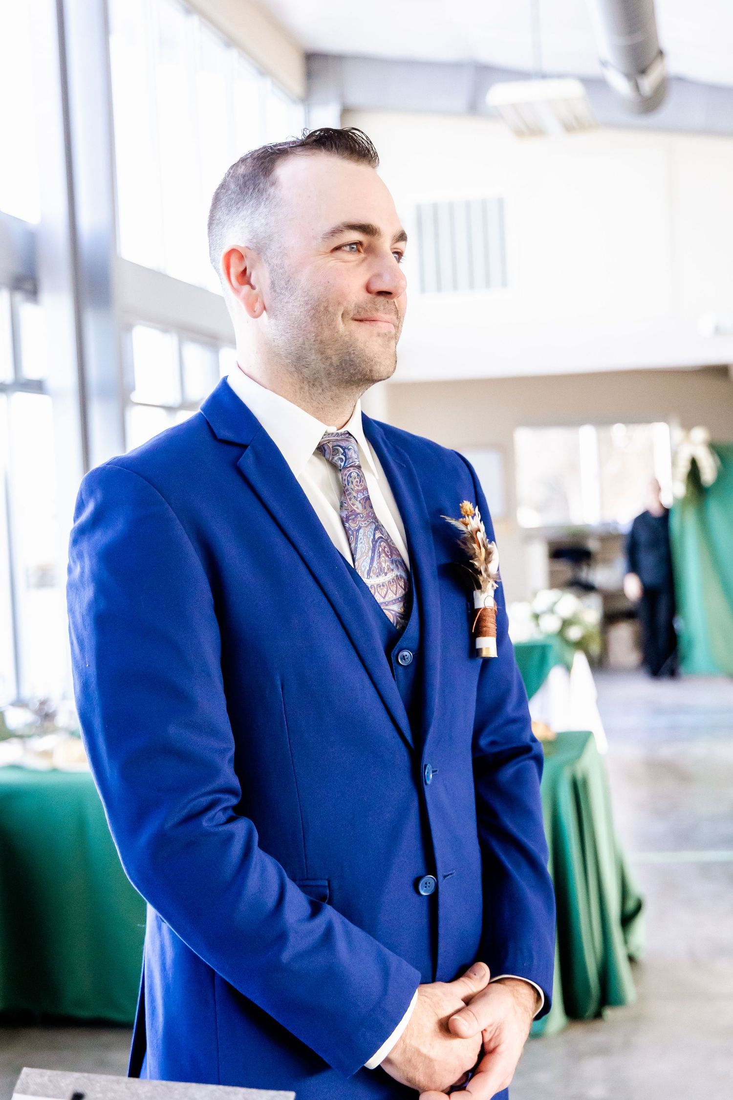 Groom in royal blue suit with floral boutonniere smiles during wedding reception.