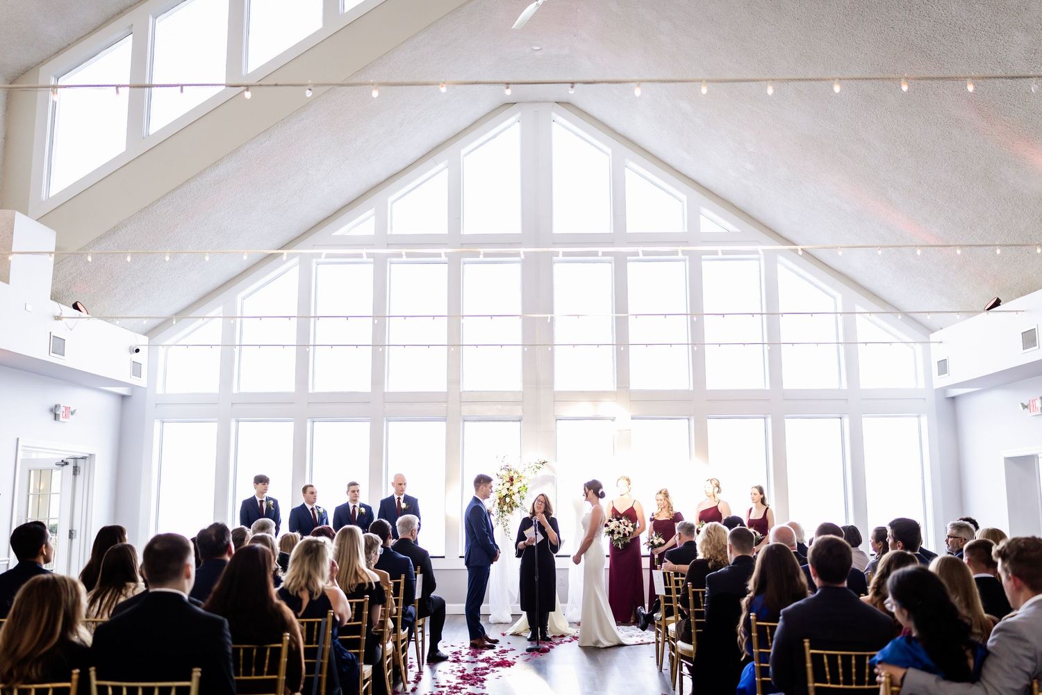 Wide view of a bright white wedding venue with guests seated for the ceremony.