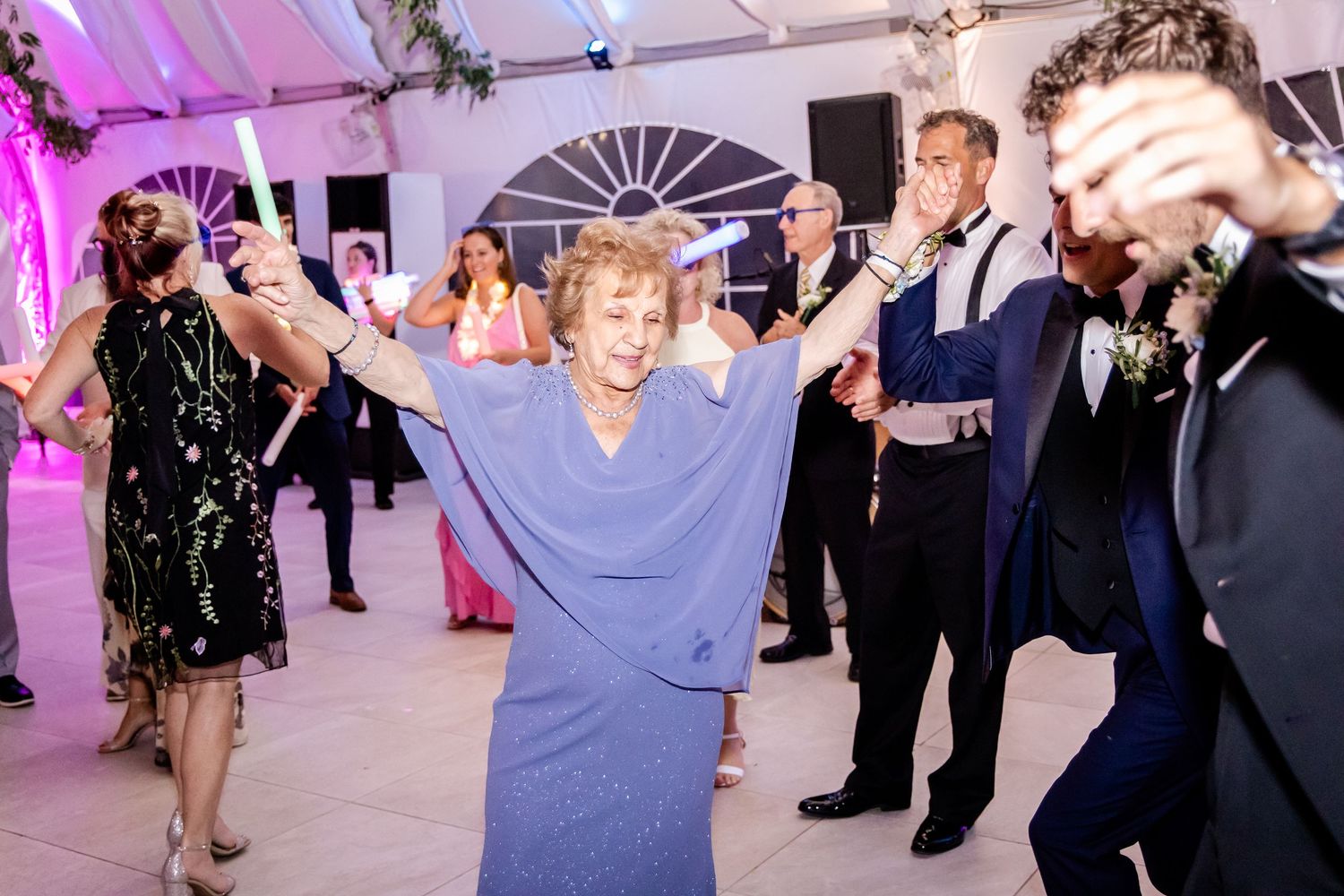 Wedding reception dance floor illuminated with purple lighting and white fabric ceiling draping.