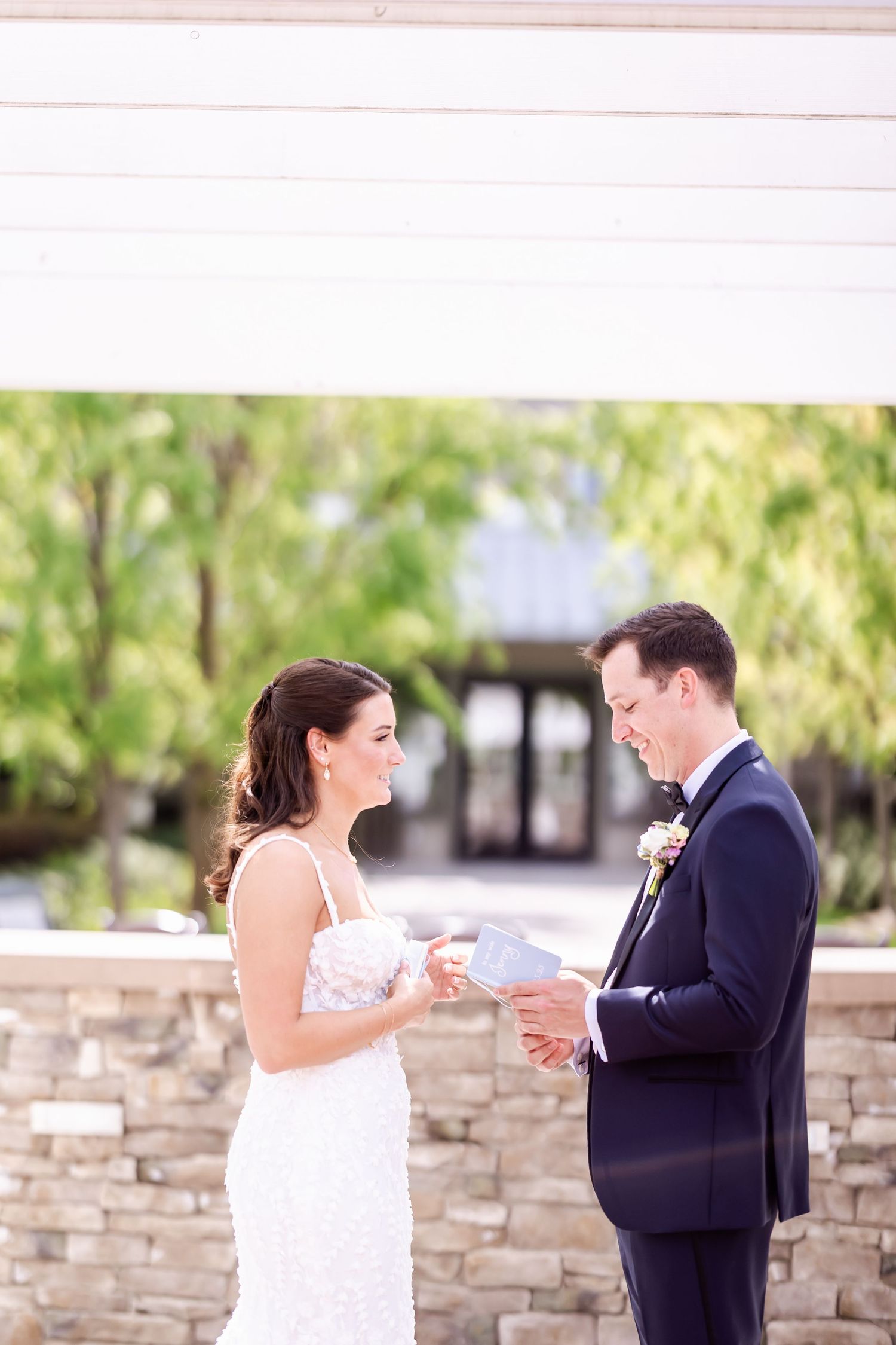 A couple exchanges vows during their outdoor wedding ceremony next to a stone wall.