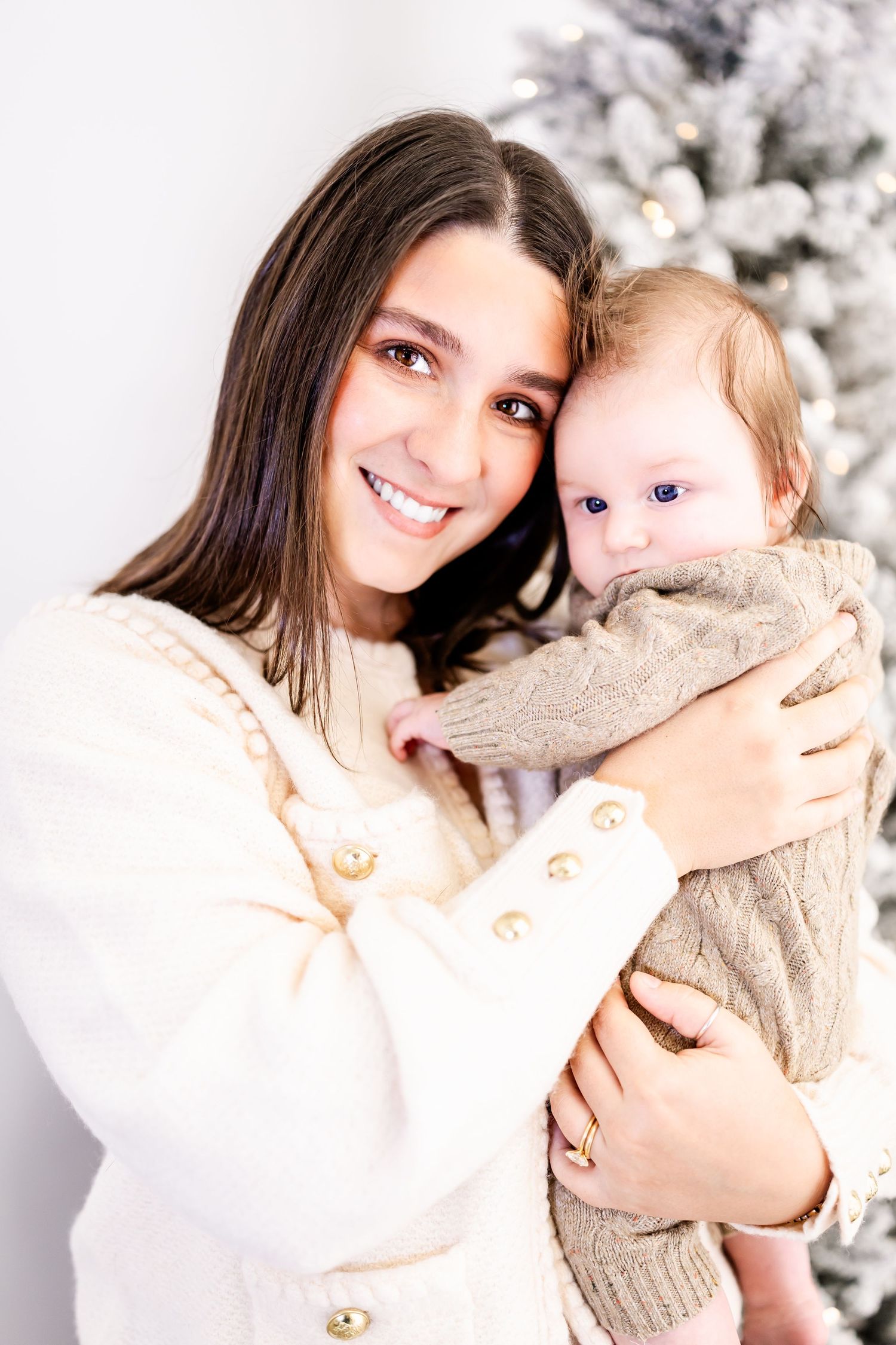 Heartwarming portrait of a loving embrace between parent and baby with a snowy white Christmas tree backdrop.