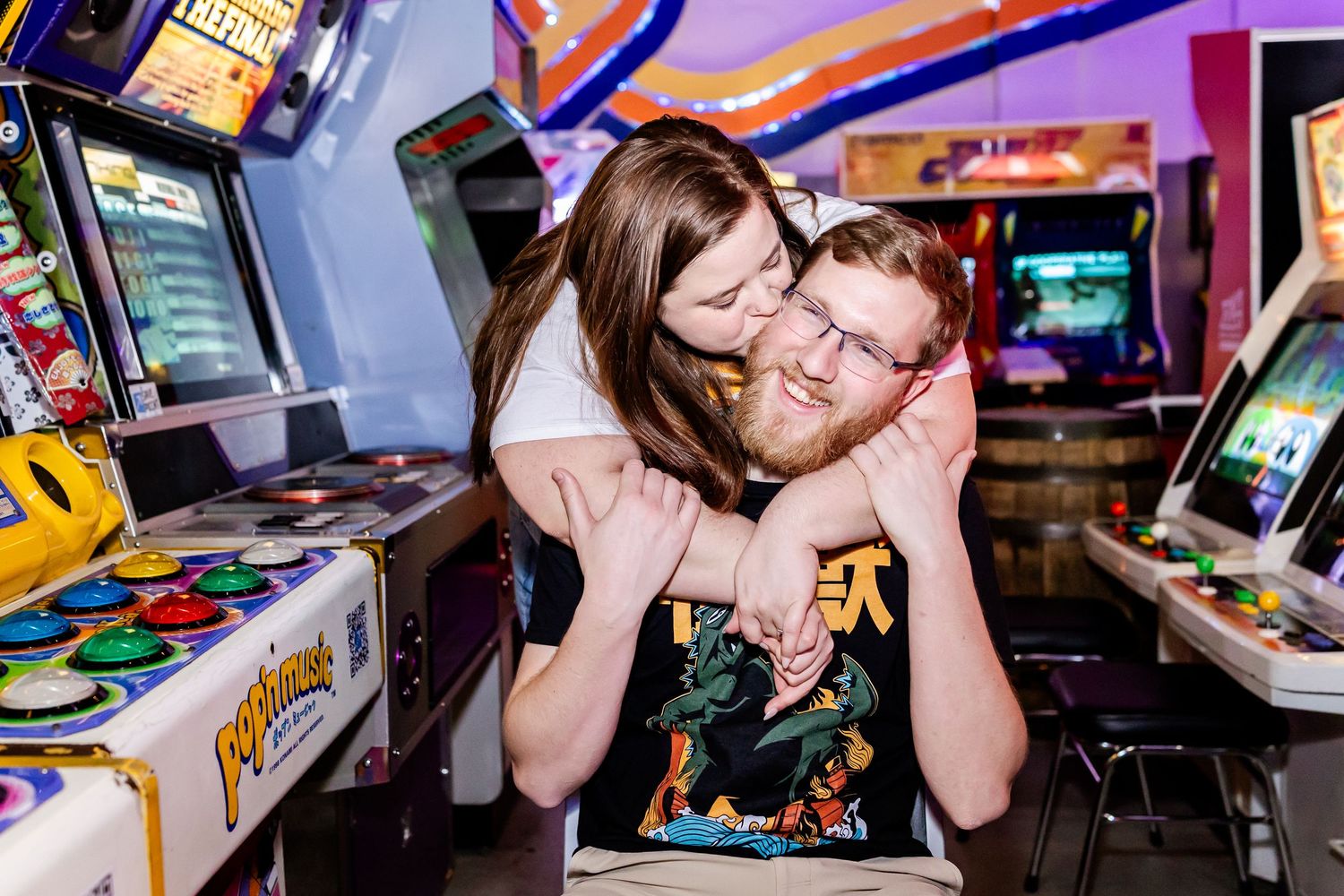 Couple sharing an affectionate moment while playing arcade games in a retro gaming arcade with colorful machines.
