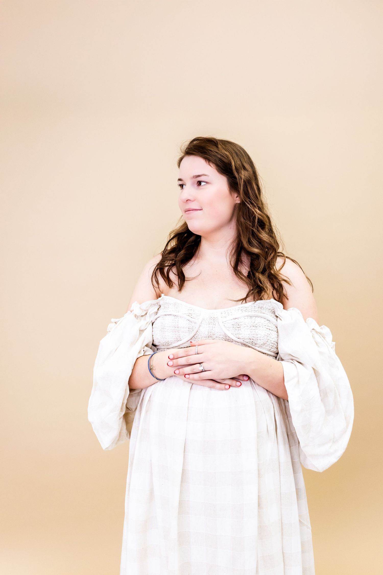A person in a romantic white off-shoulder dress with long sleeves poses against a beige backdrop.