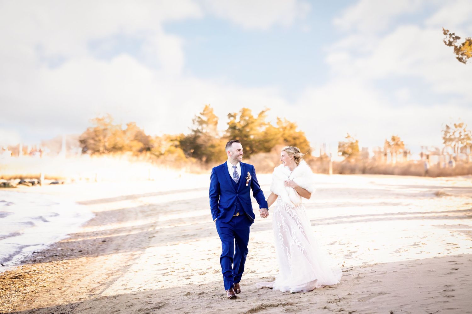 Wedding couple walking hand in hand on a snowy winter path in formal attire.