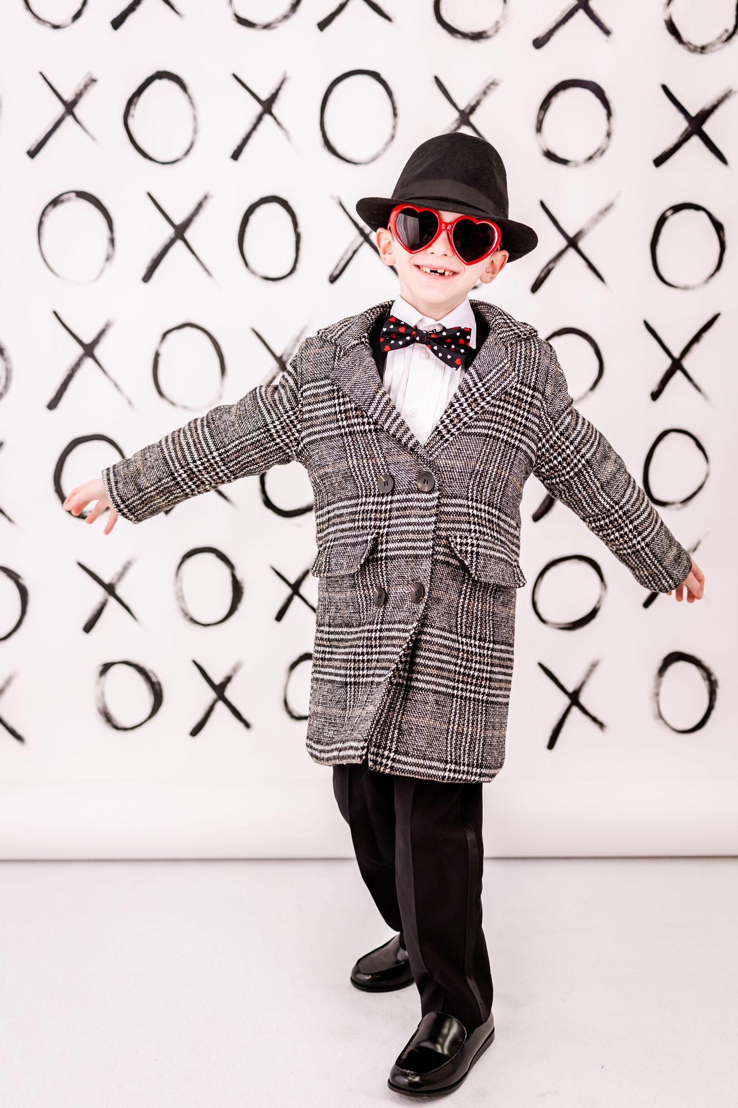 Stylish outfit featuring plaid overcoat, bow tie and red sunglasses against X's and O's background.