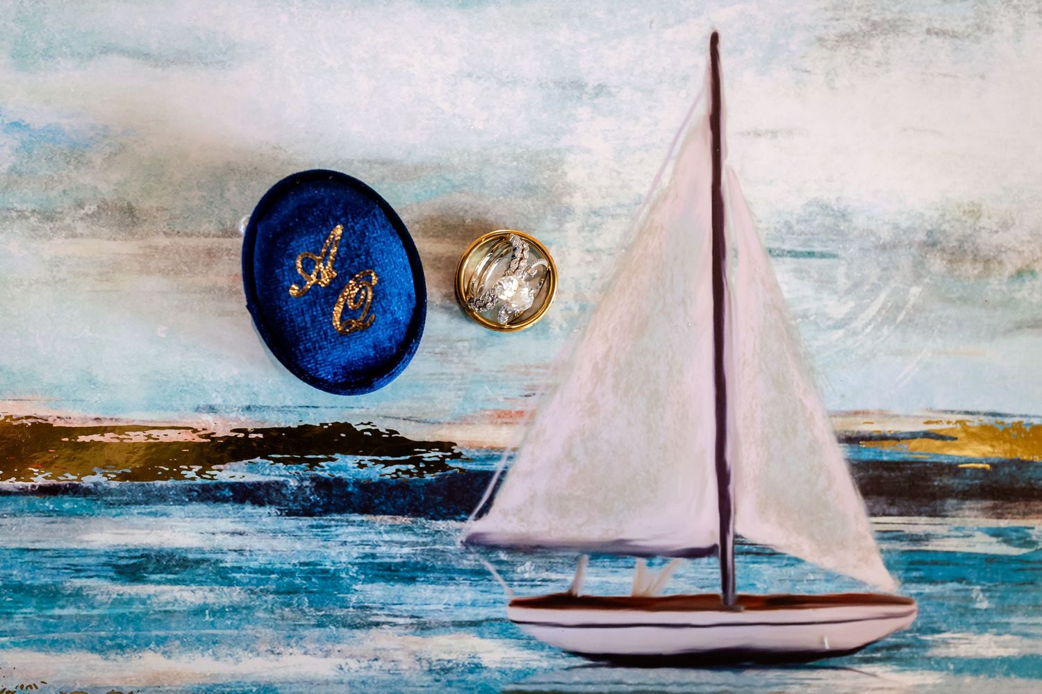 A painted sailboat scene with decorative blue and gold brooches against a watercolor seascape background.