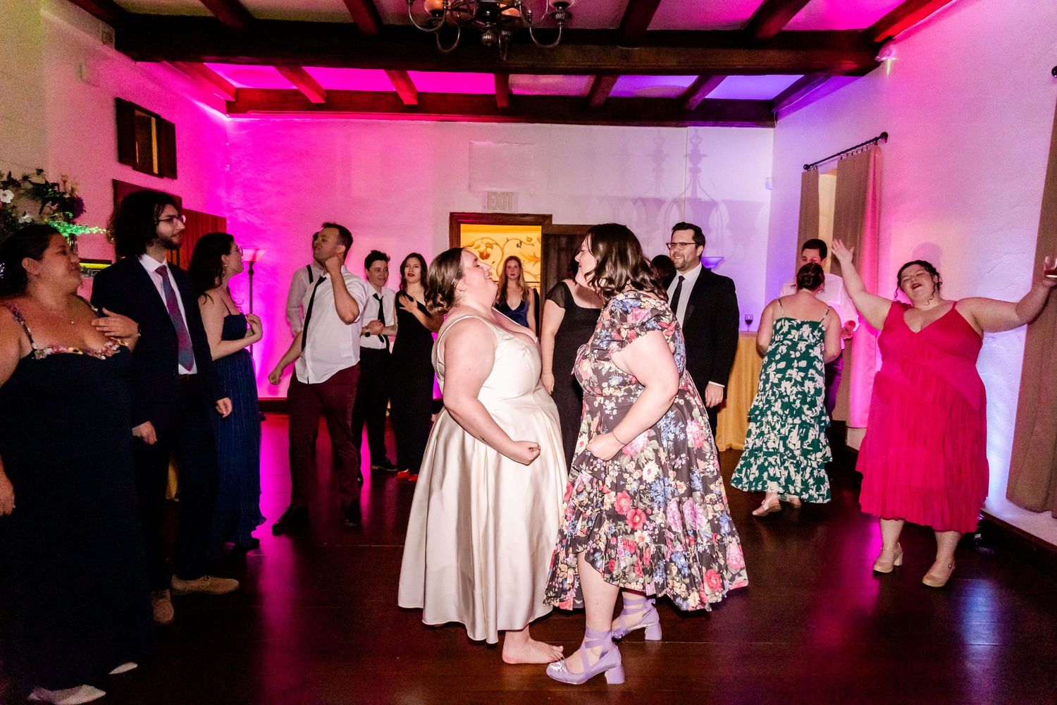 Wedding reception dancers move to the music under pink and purple mood lighting.