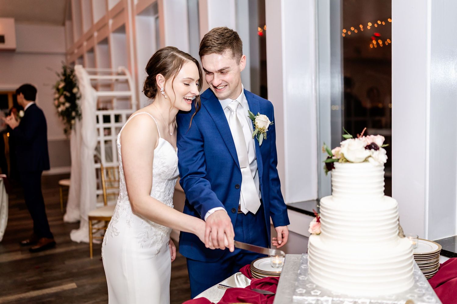 Wedding couple cutting their elegant white tiered cake during reception celebration.