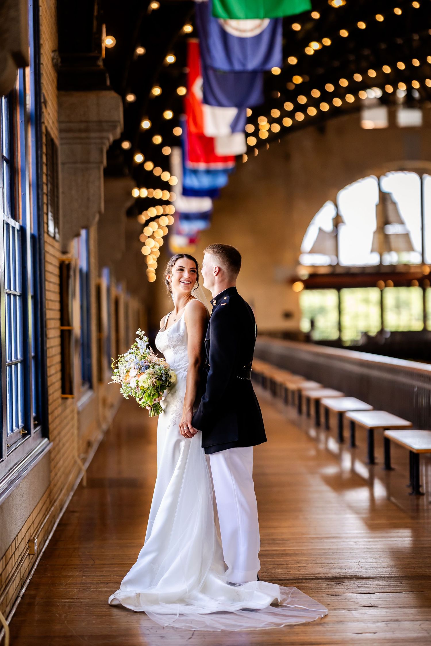 Romantic wedding couple shares intimate moments in a rustic venue hallway with twinkling string lights overhead.