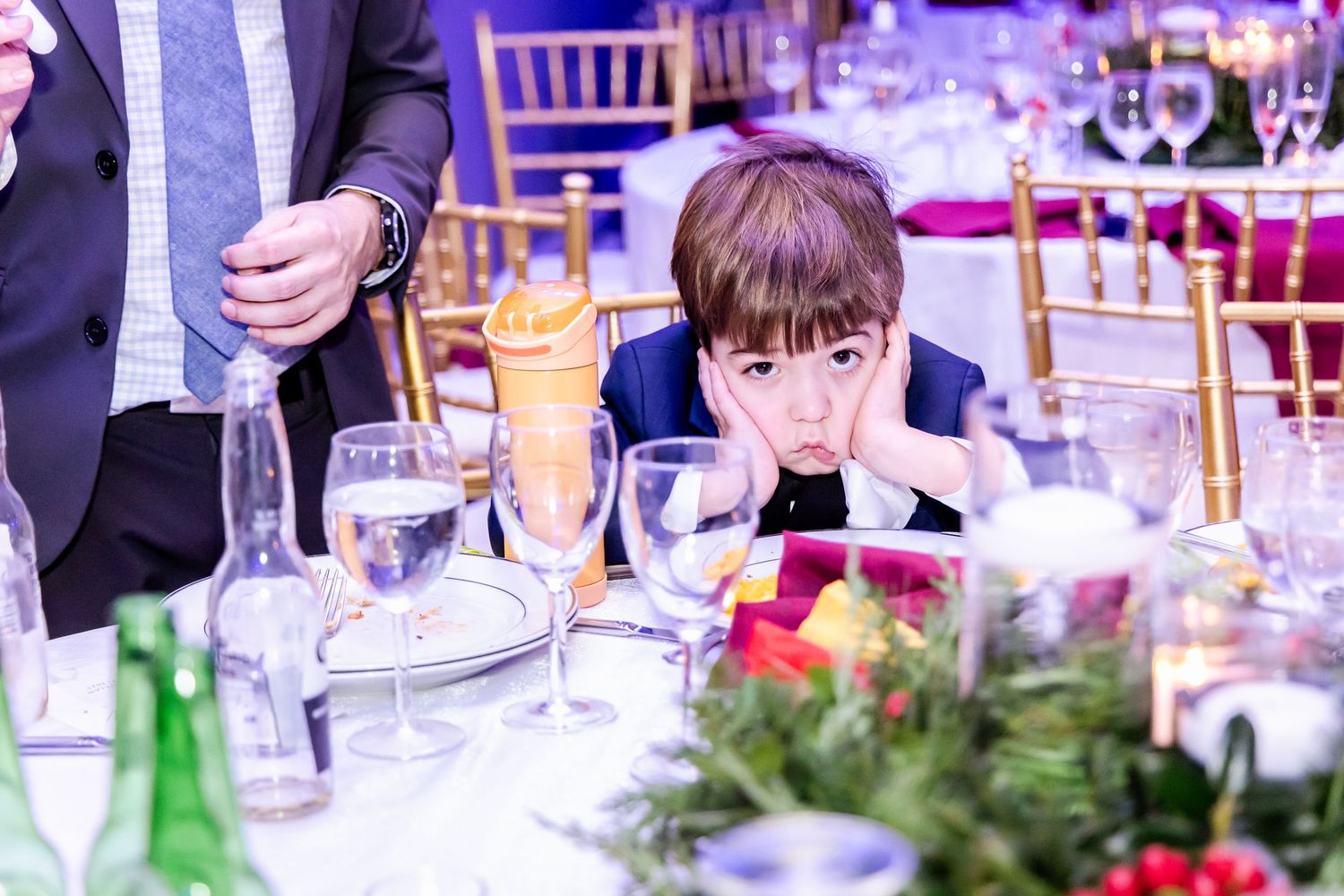 A formal dining event with tables decorated in red and white floral centerpieces under purple ambient lighting.