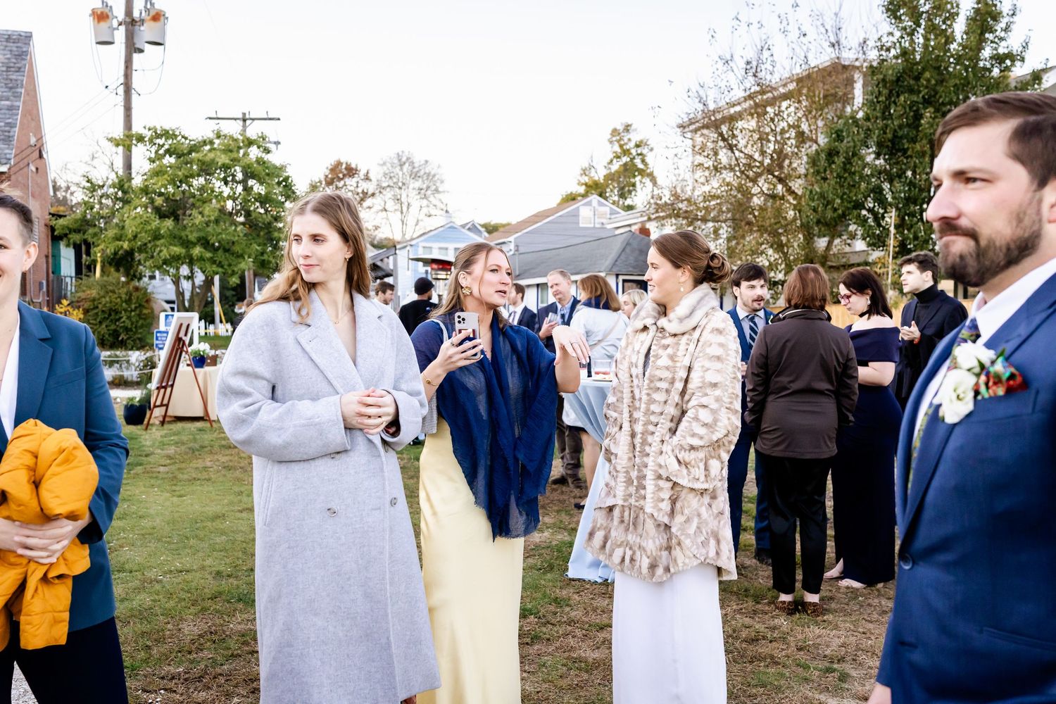 Guests mingling outdoors at an elegant wedding reception, dressed in formal attire on a green lawn.