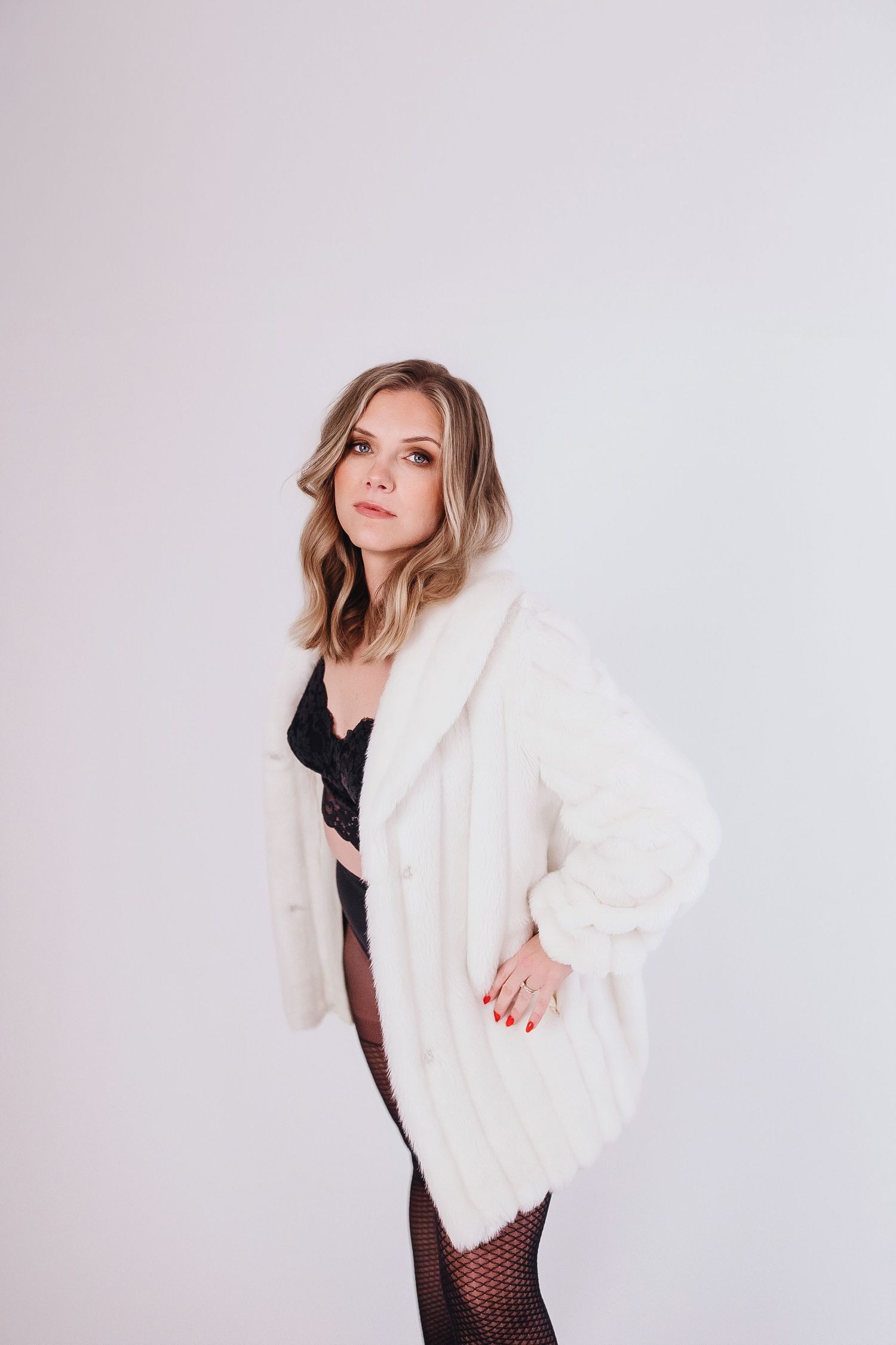 Fashion model poses in white cardigan and black lingerie against light background.