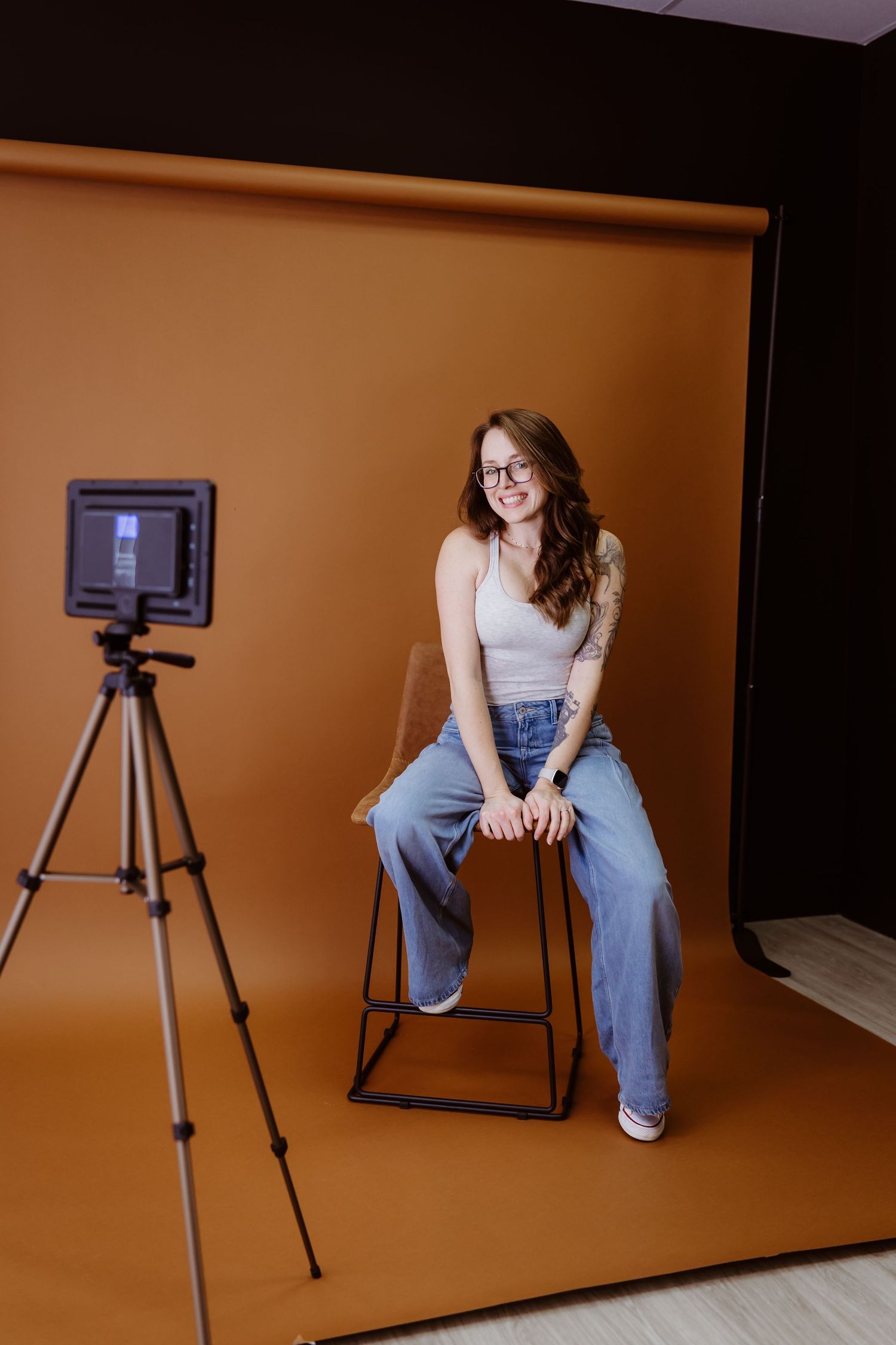 A studio photography setup with camera equipment and seating against an orange backdrop.