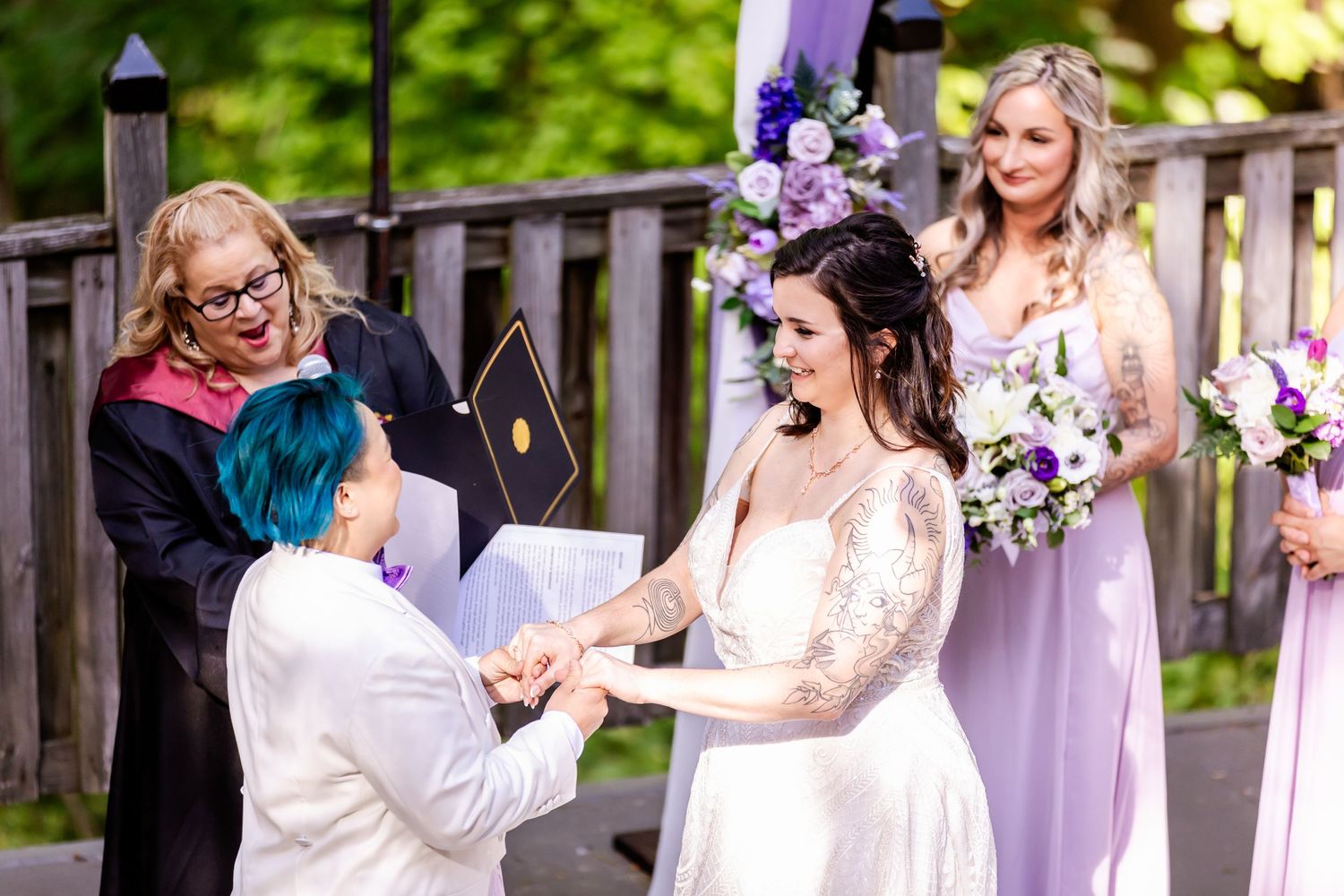 Two people exchange vows during an outdoor ceremony with purple decor and floral arrangements.