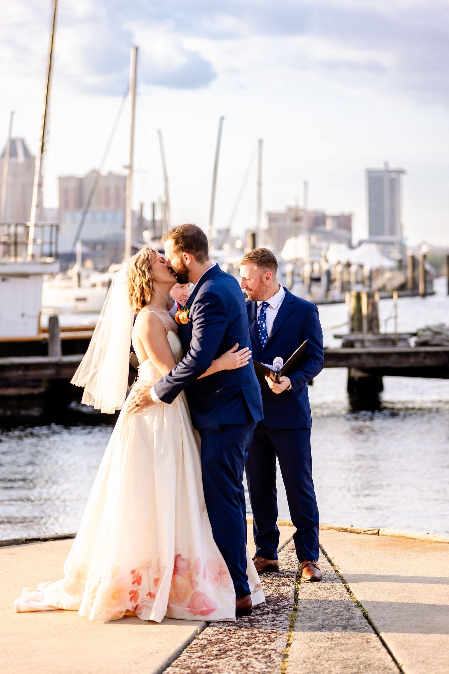 A romantic waterfront scene at a marina with boats and city buildings in the background.
