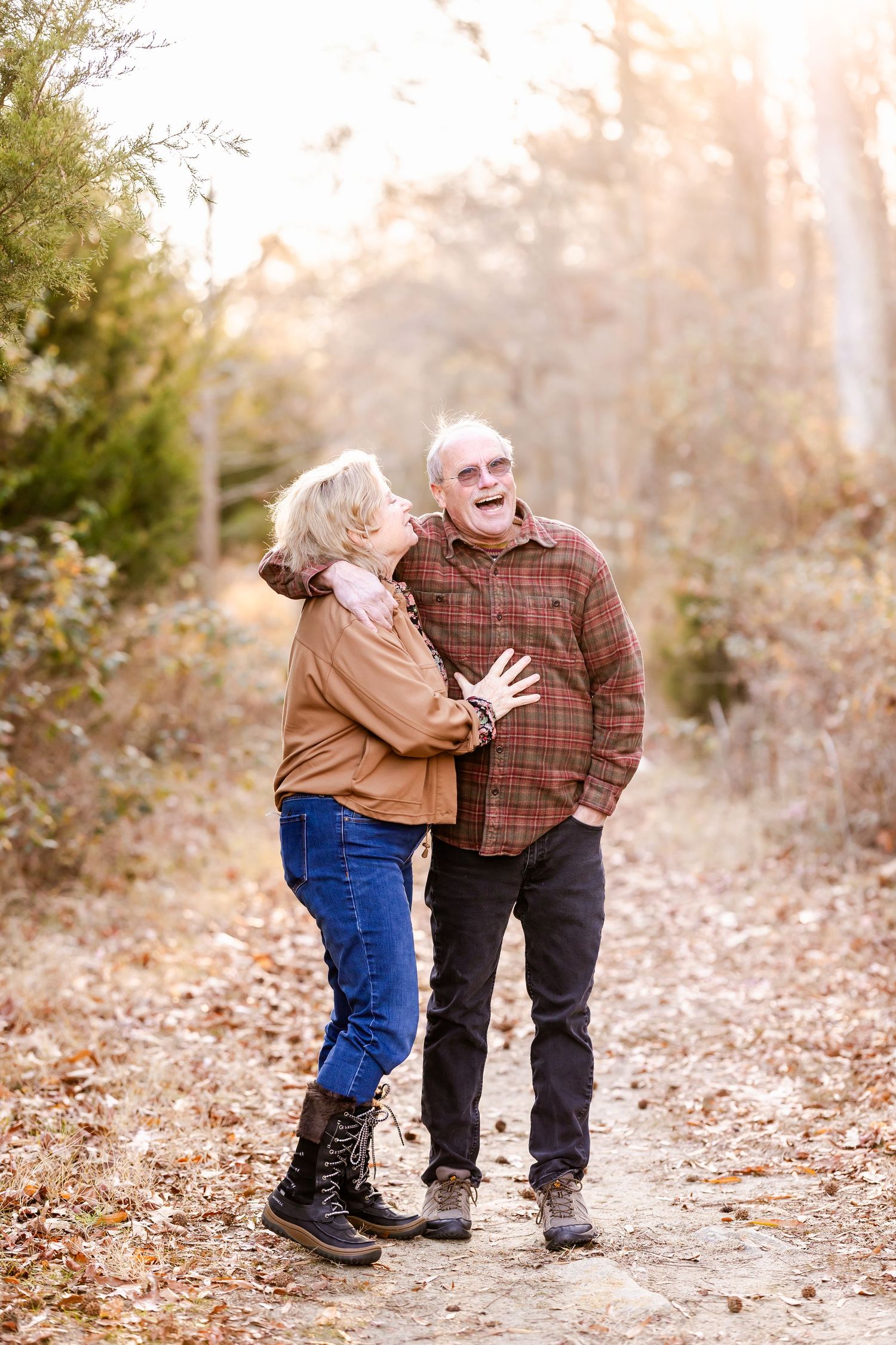 A couple shares a joyful moment while walking on a leaf-covered autumn trail.