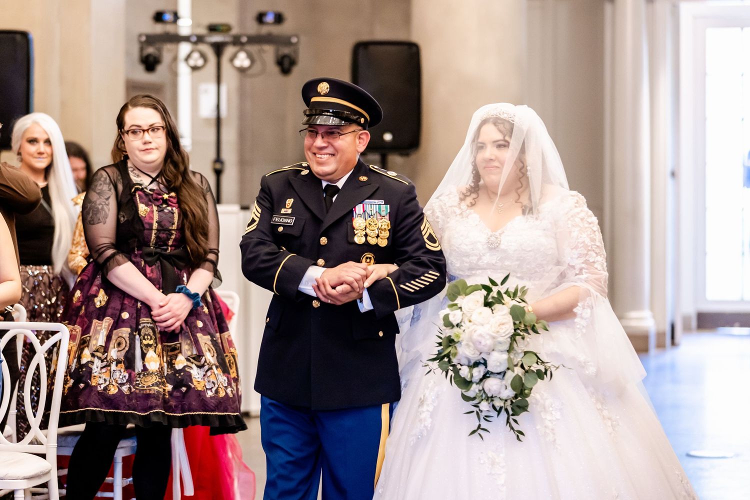 Military service member in dress uniform escorts bride in white gown down wedding aisle.