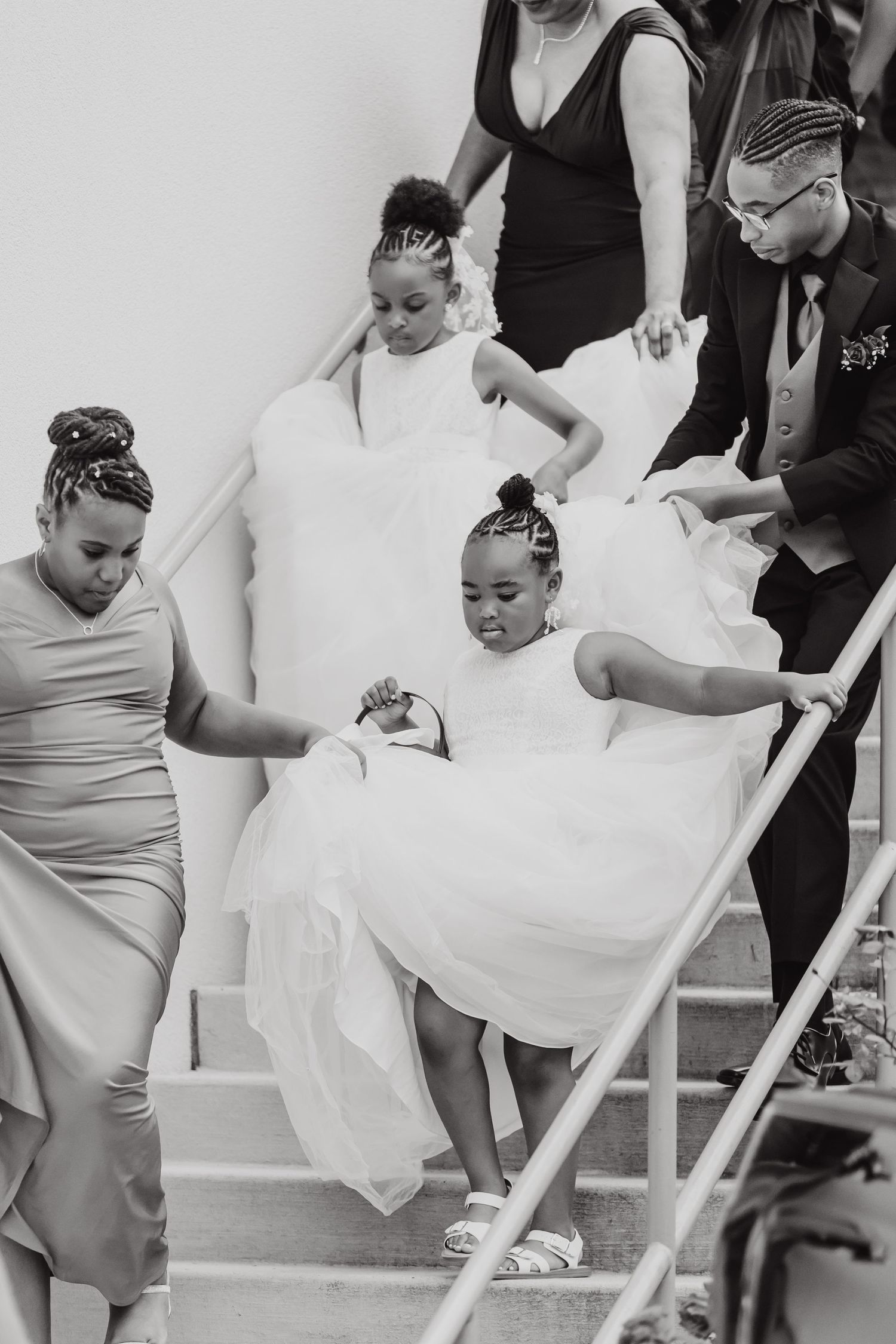 Wedding party descending white stairs while helping someone in a flowing white dress.