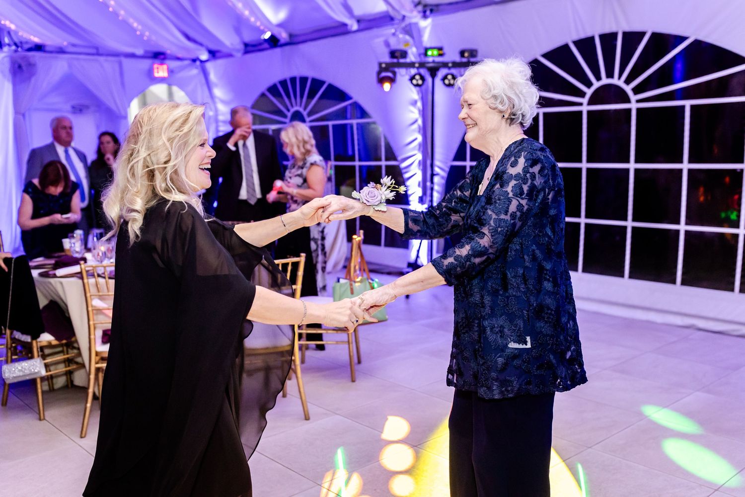 Wedding guests dancing under purple lighting and elegant white draped ceiling.