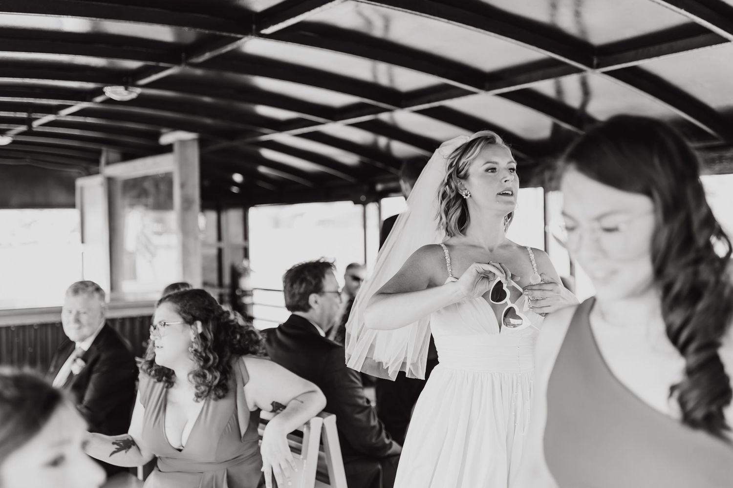 A candid black and white photograph captured during a wedding reception shows guests enjoying themselves on a covered porch.