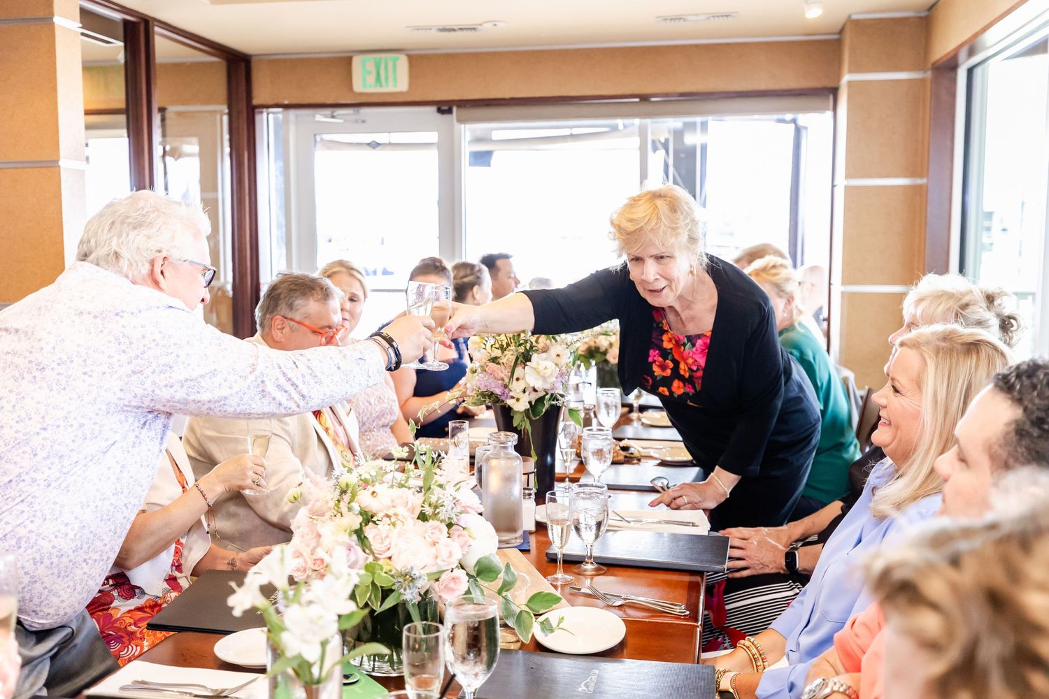Celebratory gathering with guests interacting around a formal table setting with white floral arrangements.