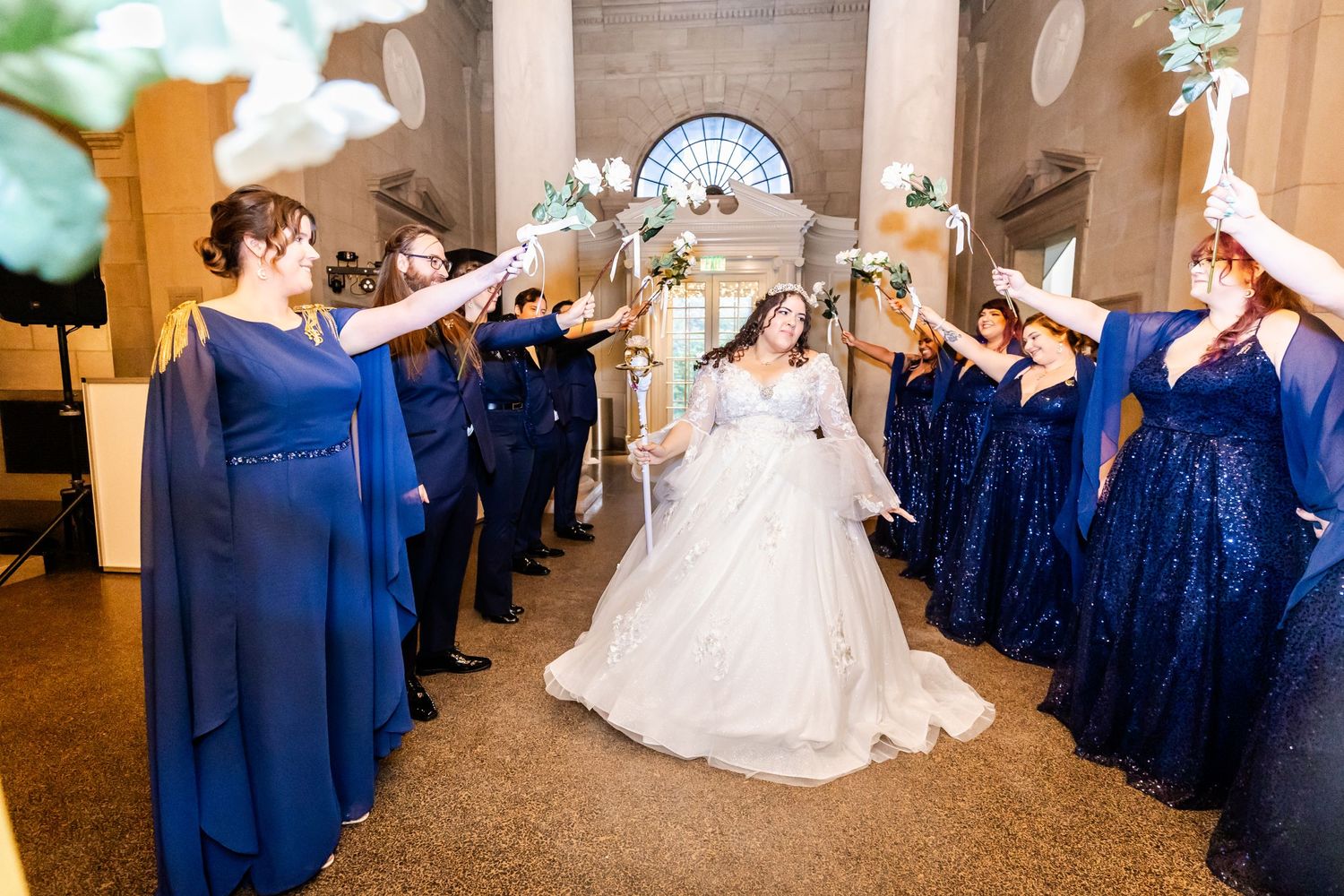 Wedding party forms sparkler exit tunnel in navy blue attire inside elegant venue.