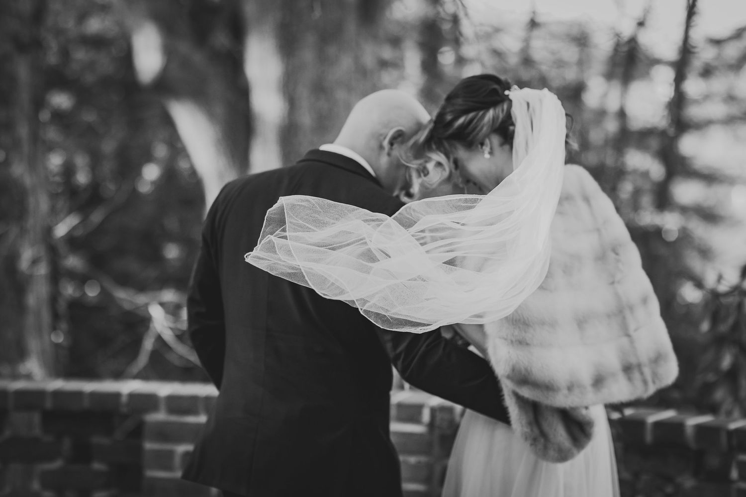 A romantic black and white wedding photo shows a tender moment between a couple as the bride's veil flows in the breeze.