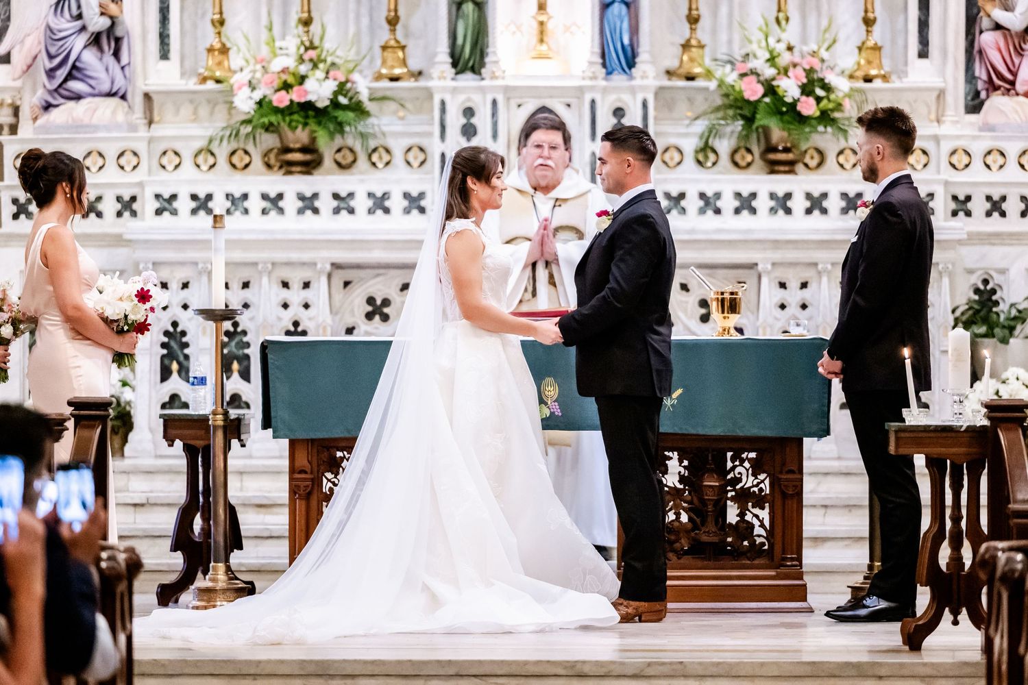 Elegant church interior with ornate decorations and religious statues serves as backdrop for wedding ceremony.
