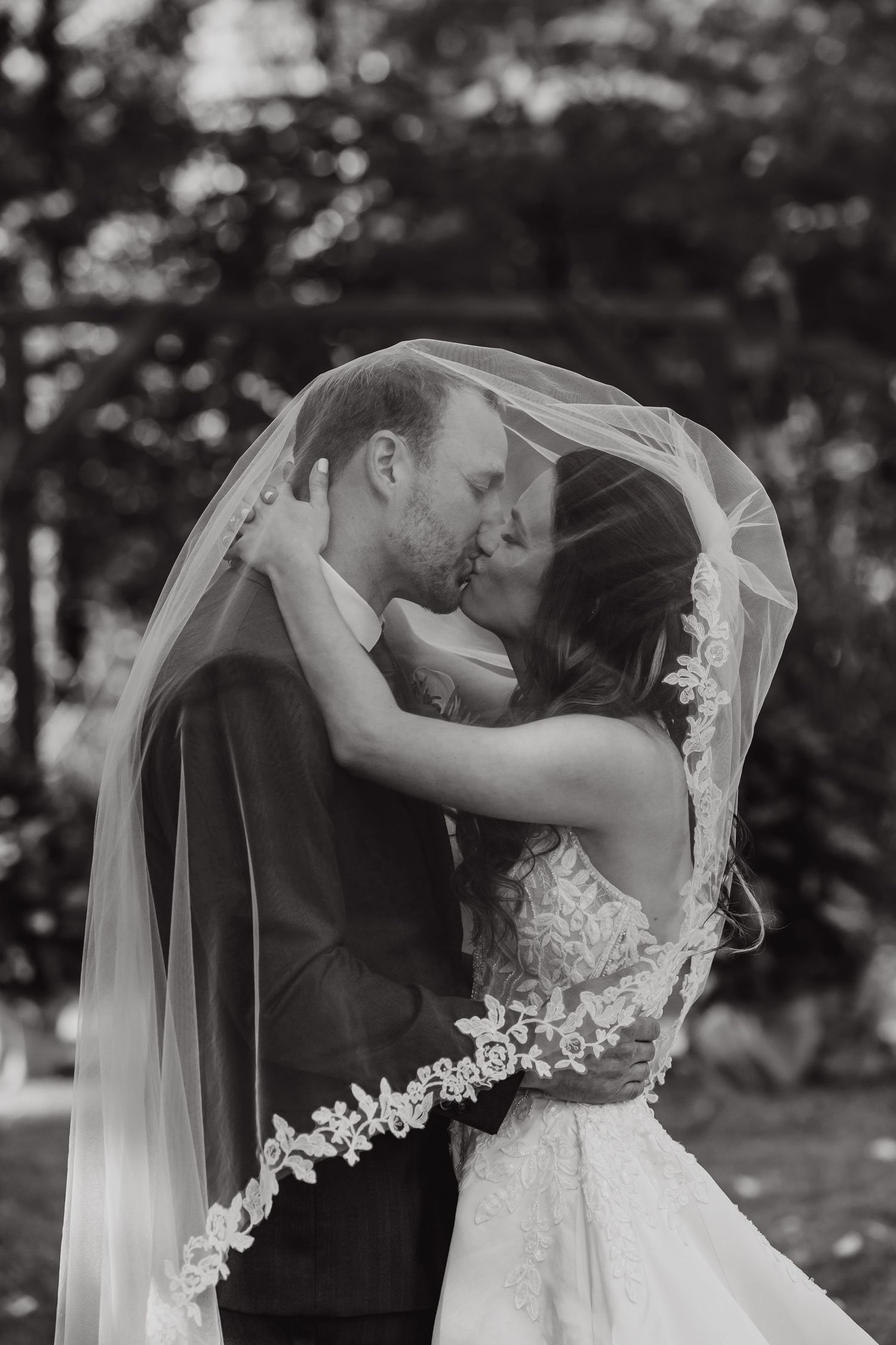 A black and white capture of a tender wedding moment under a delicate lace veil.
