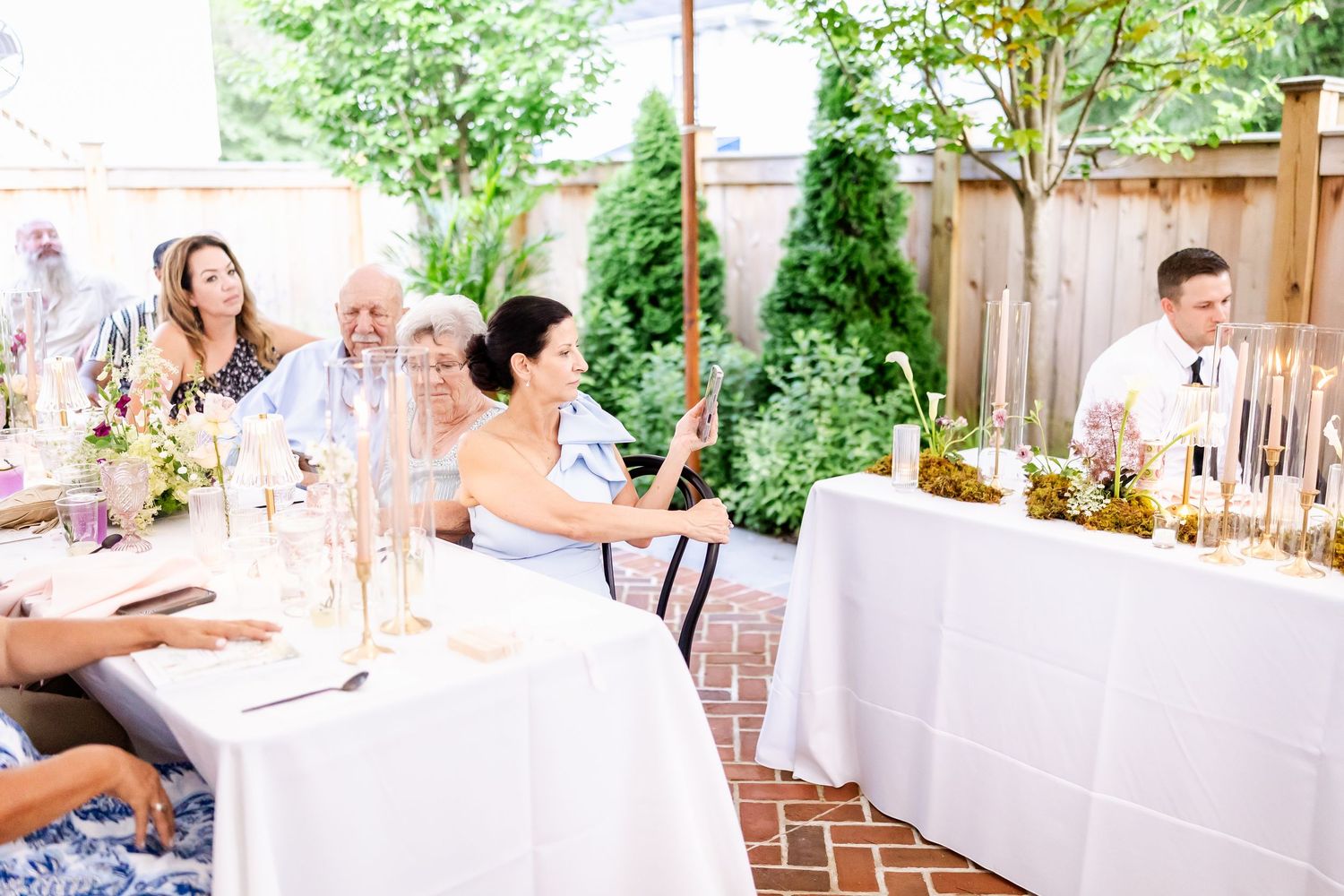 Wedding guests enjoy an outdoor reception at decorated tables with white linens.