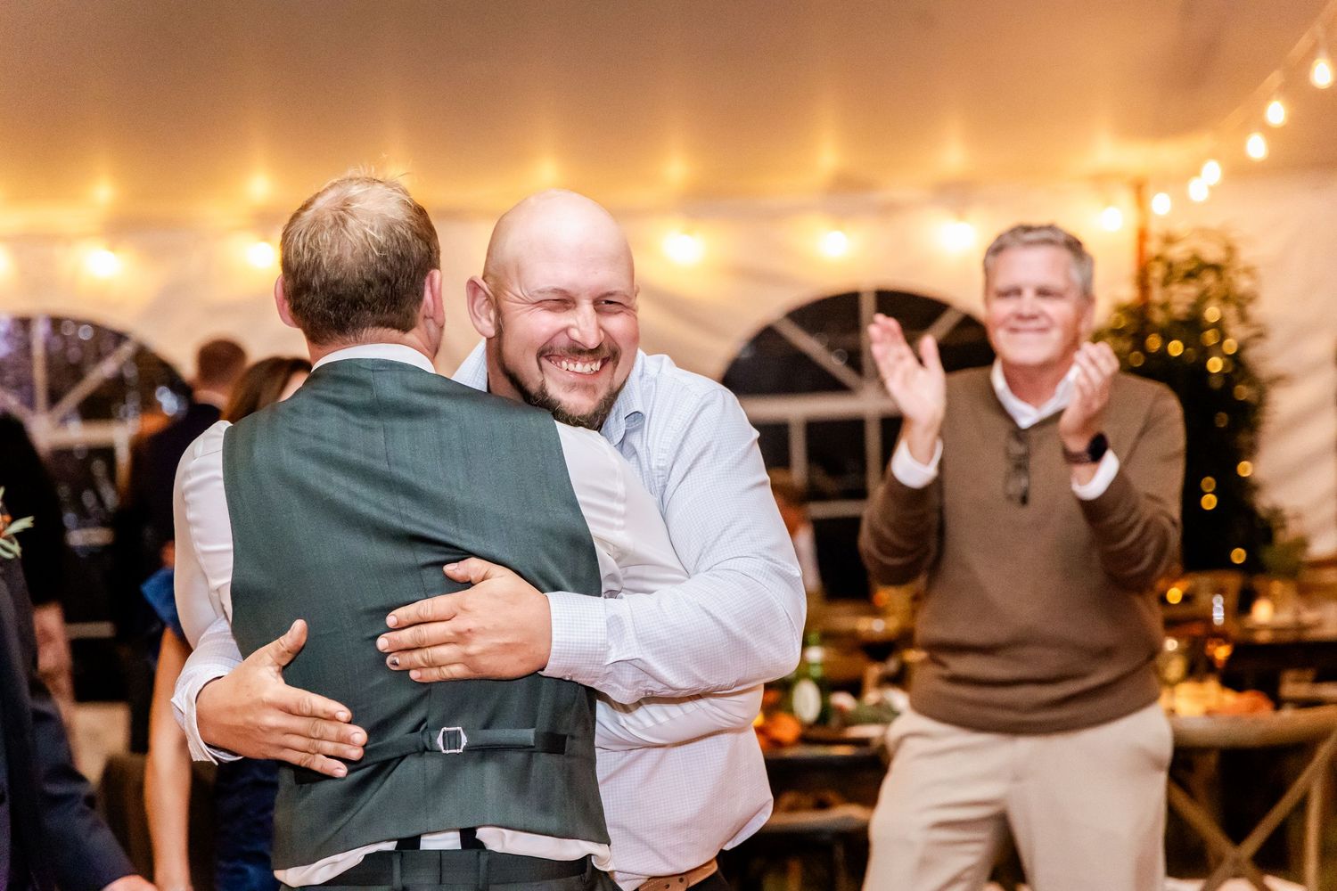 Guests dancing and celebrating at a lively wedding reception with string lights overhead.