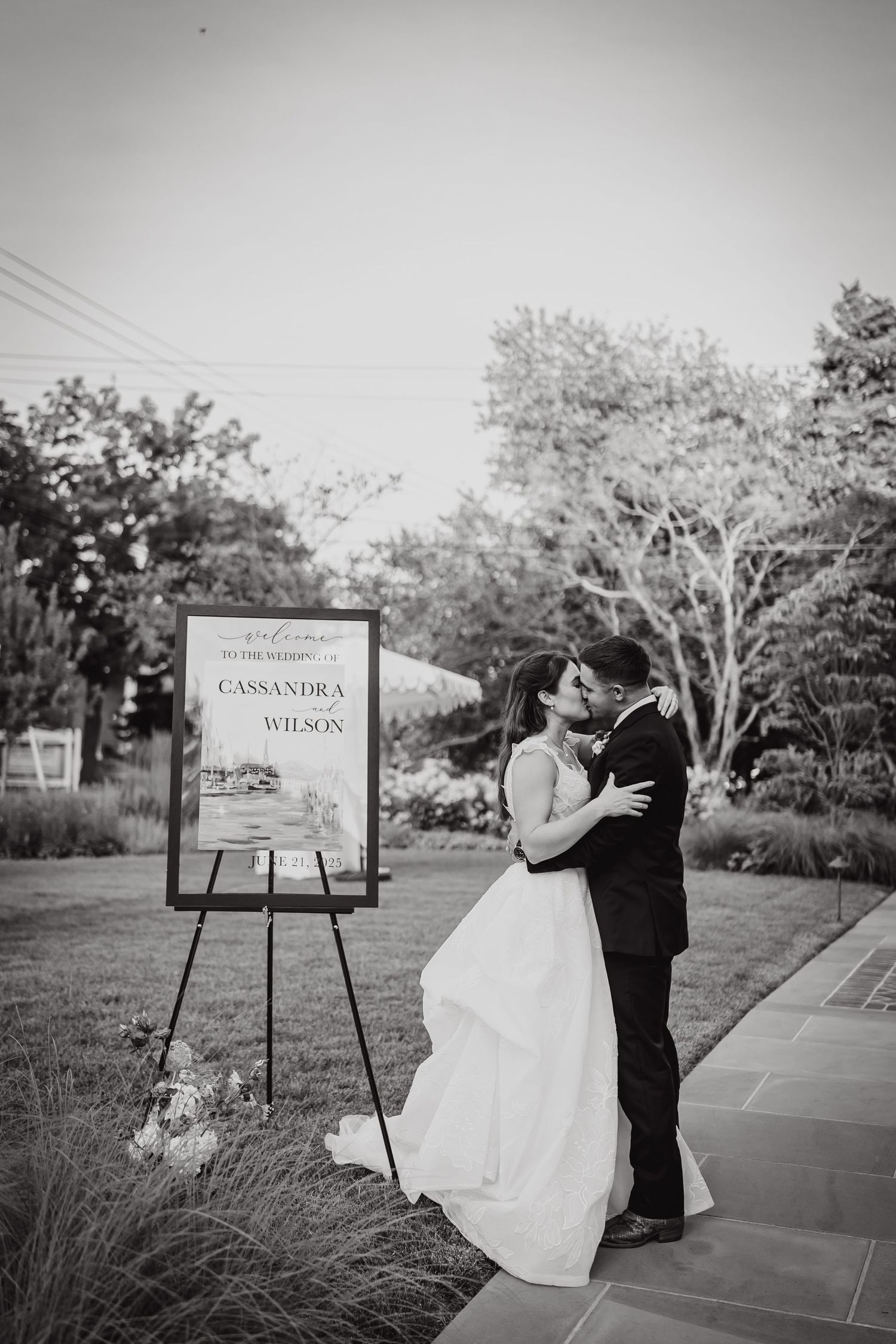 A romantic black and white wedding portrait next to a welcome sign at dusk.