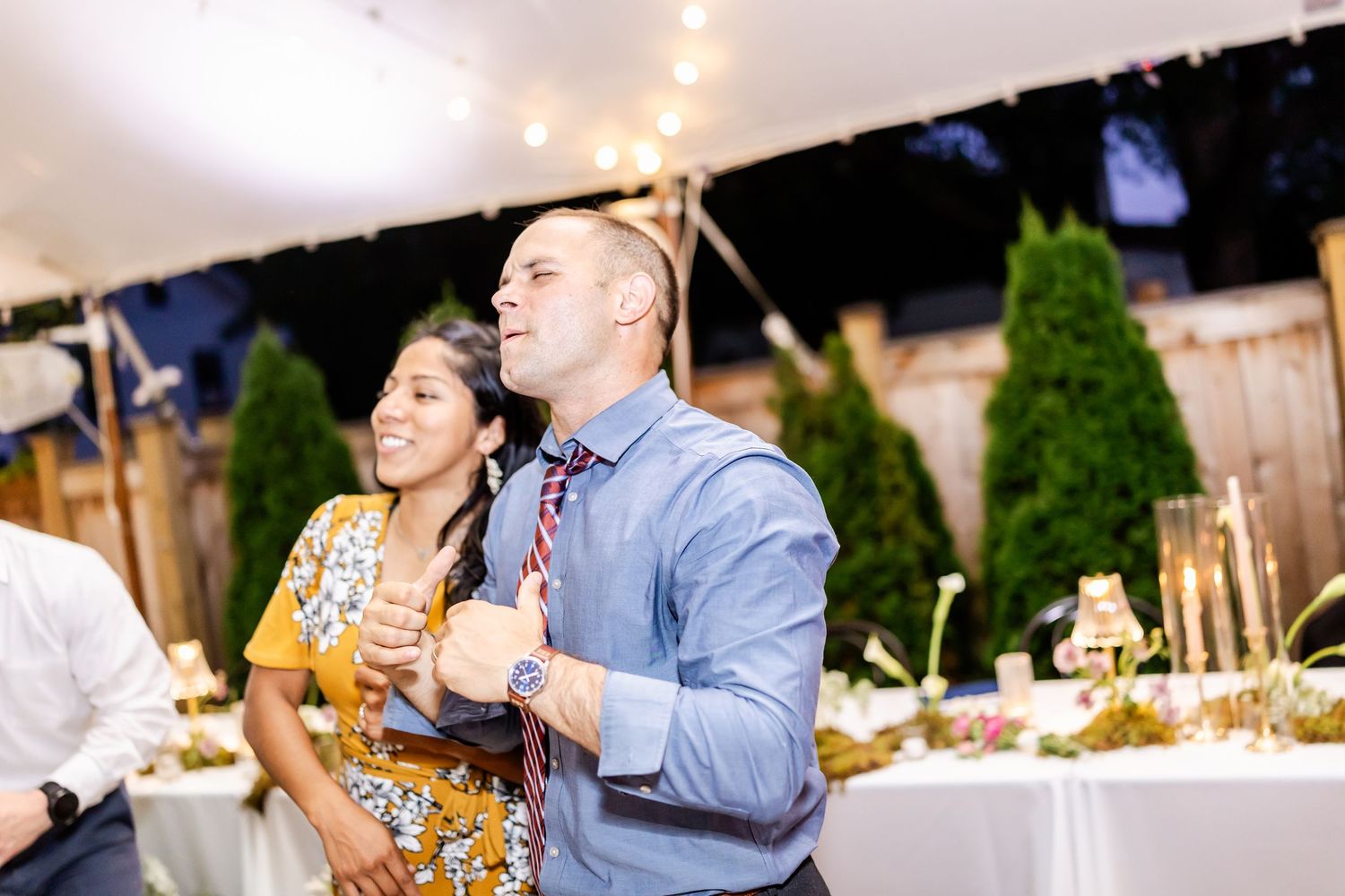 Wedding guests dancing and celebrating under a tent at an evening reception.