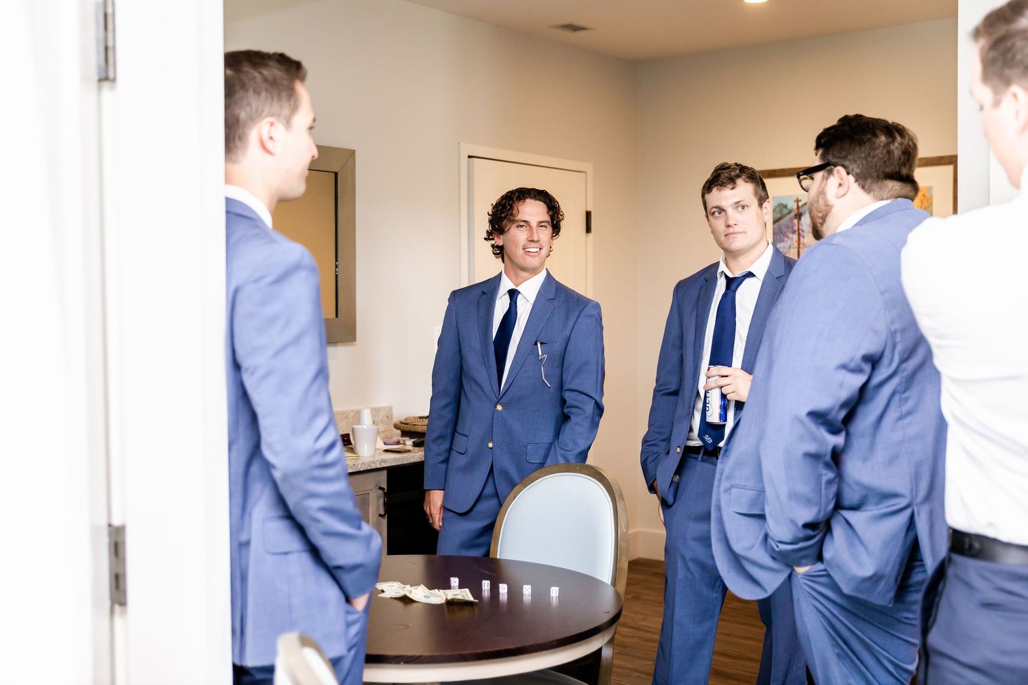 Groomsmen in matching navy suits interact around a table during pre-wedding festivities.