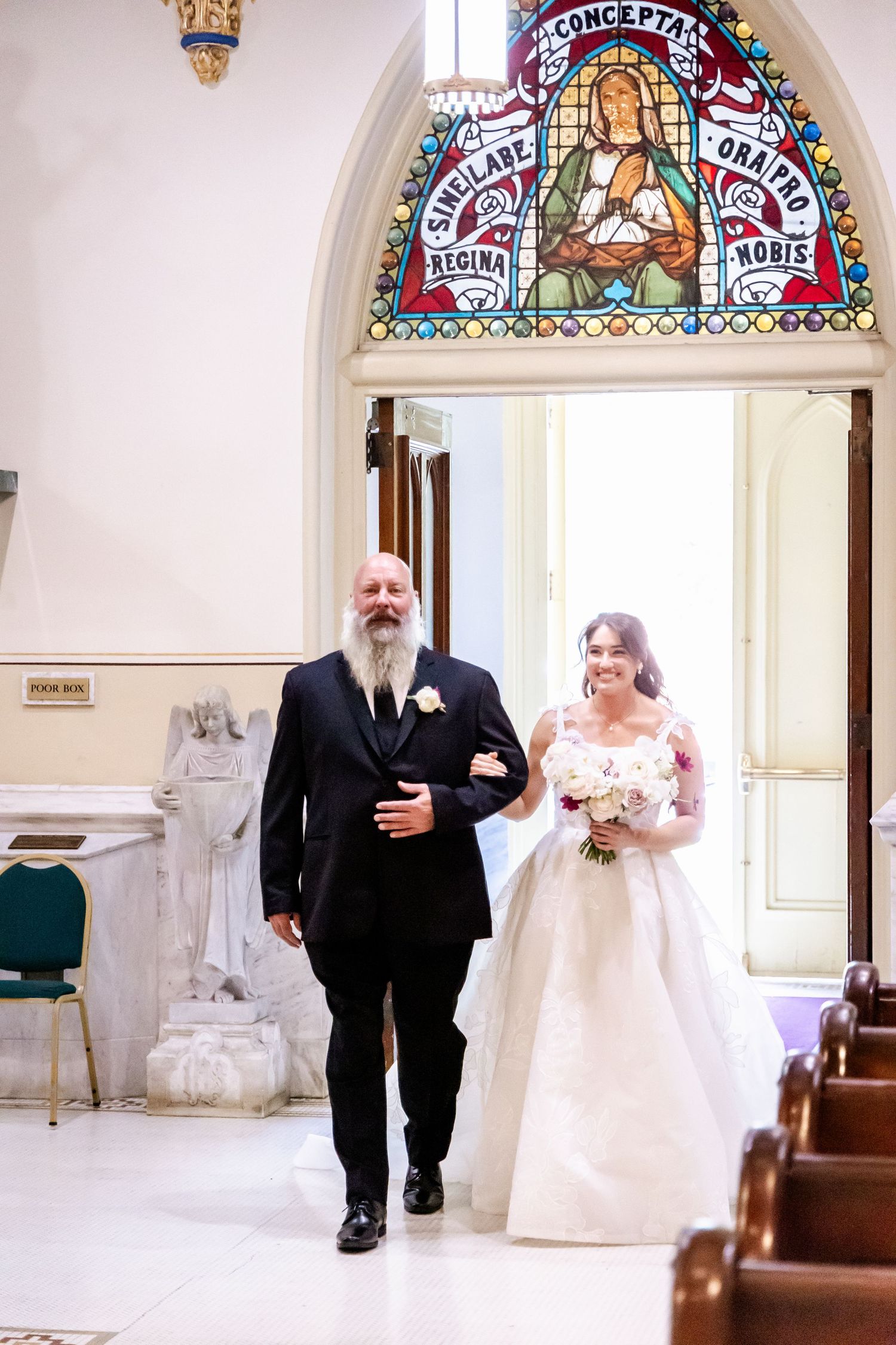 Walking down church aisle under stained glass window during traditional wedding ceremony.