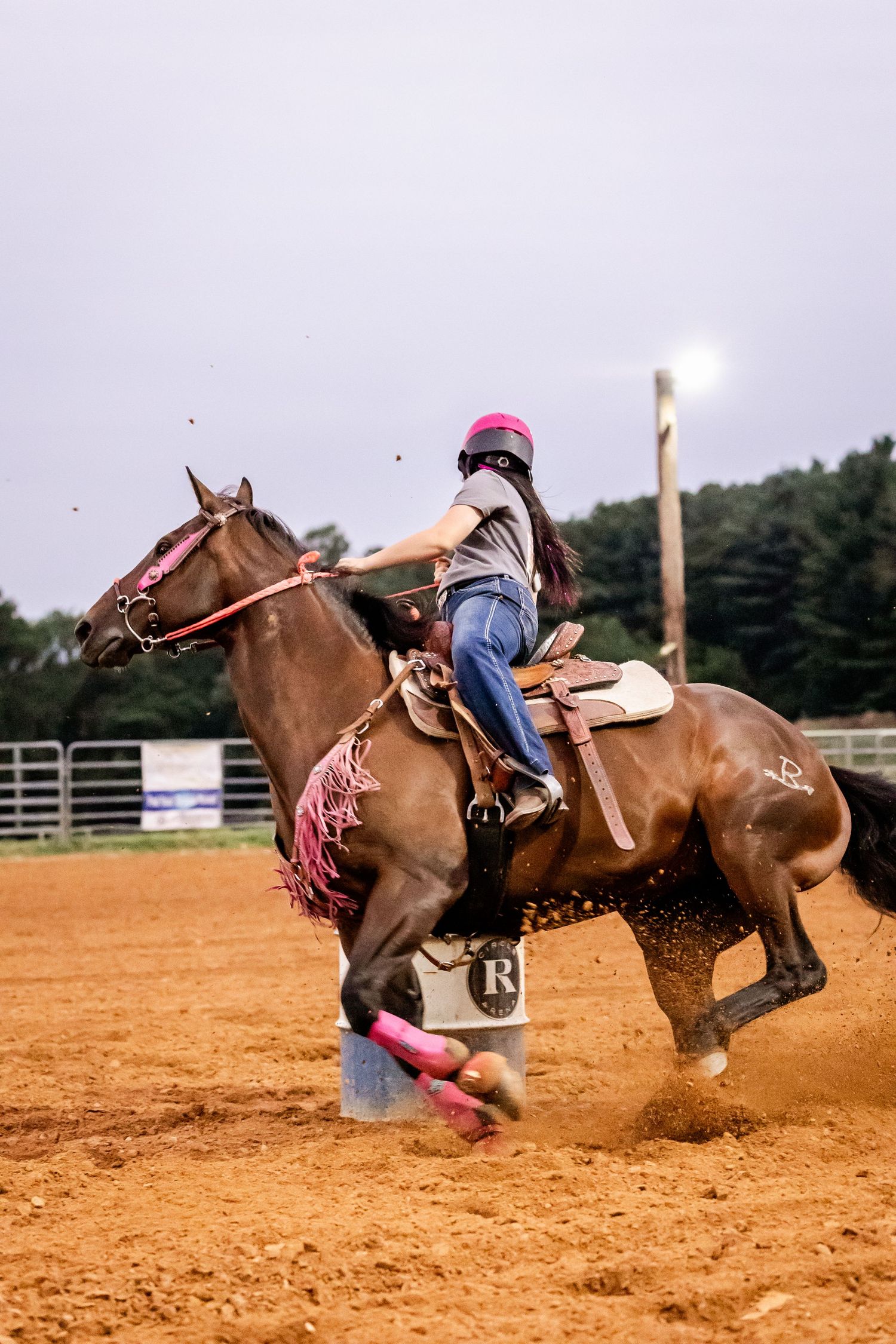 Barrel racer kicks up dust while making sharp turn in rodeo arena.
