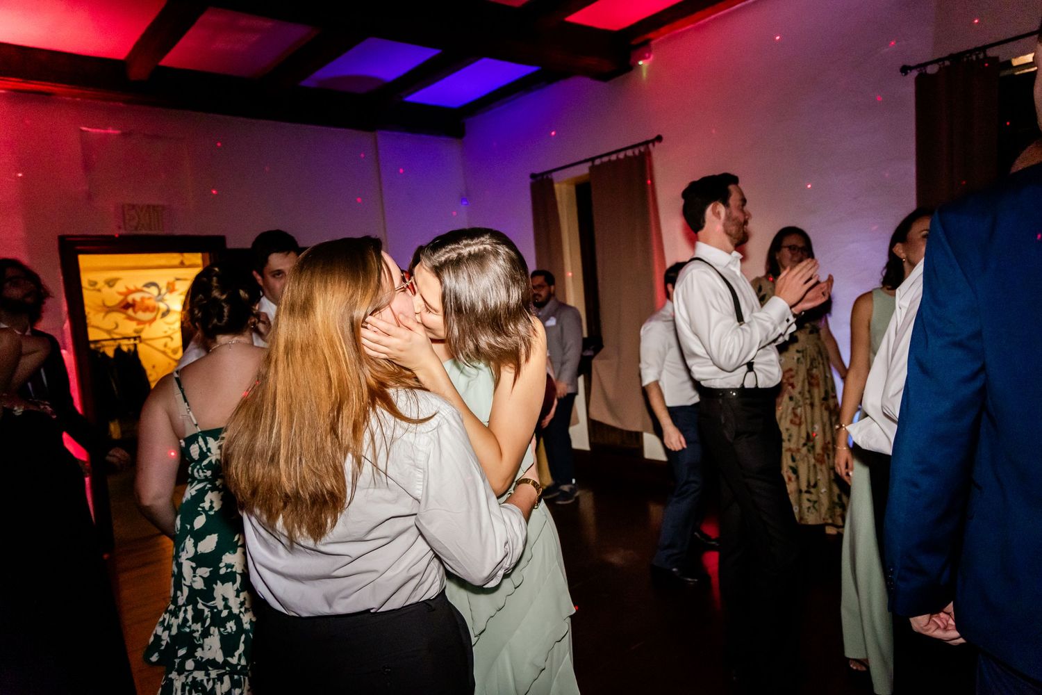 People dancing and celebrating at a reception with colorful mood lighting.