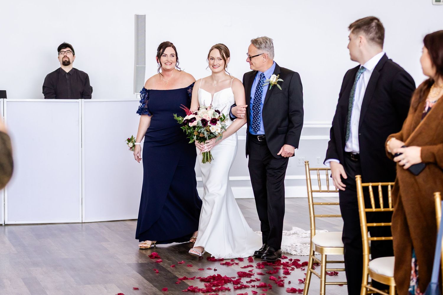 Wedding ceremony in modern venue with rose petals scattered along white aisle.