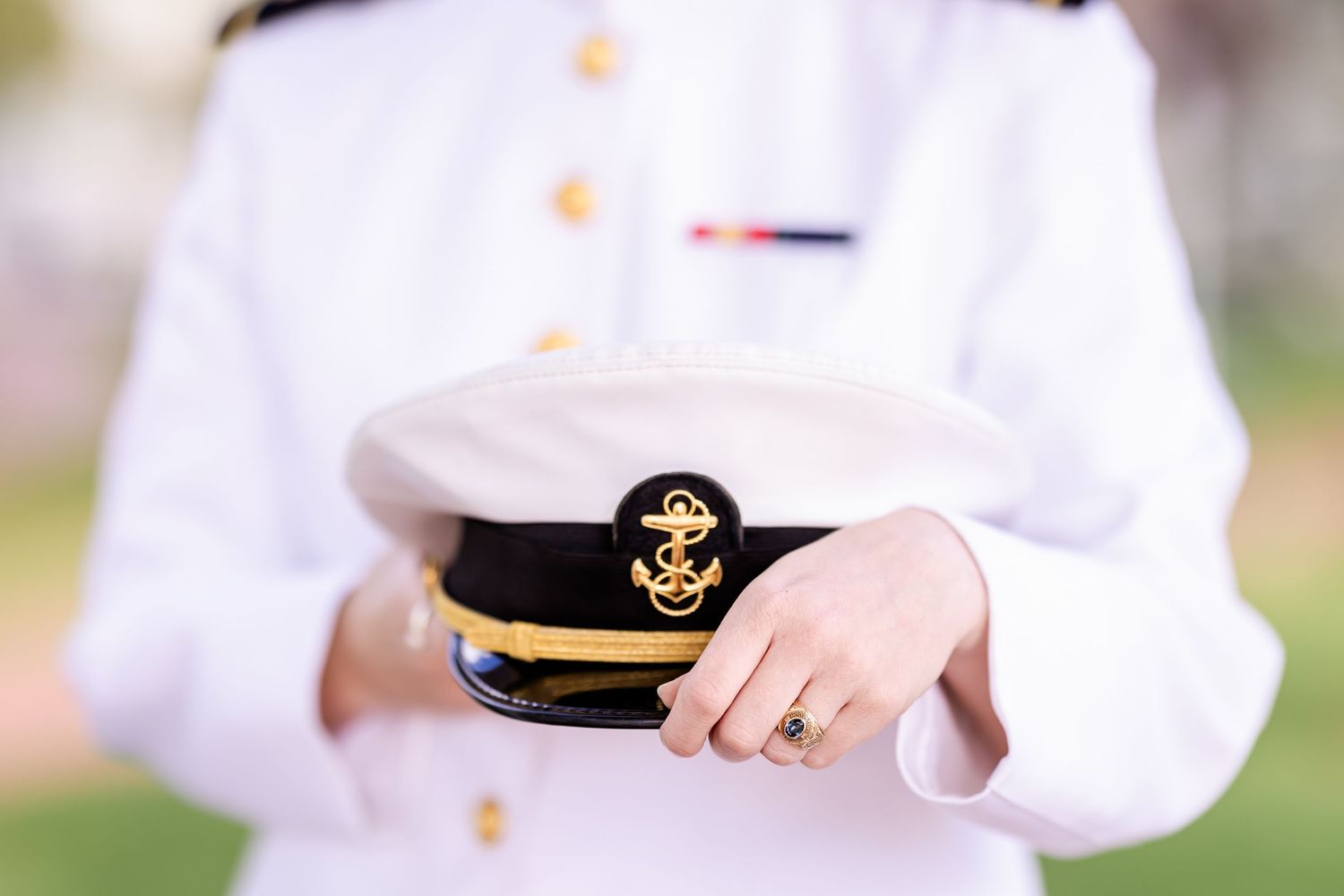 Close-up view of hands holding a white and gold naval officer's cap with anchor emblem.