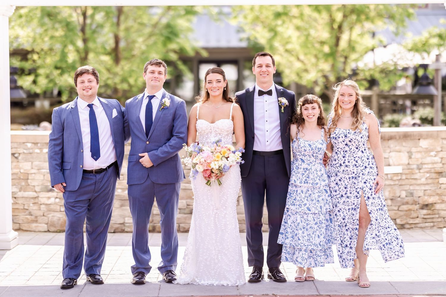 Wedding party in navy suits and floral dresses poses together on brick walkway.