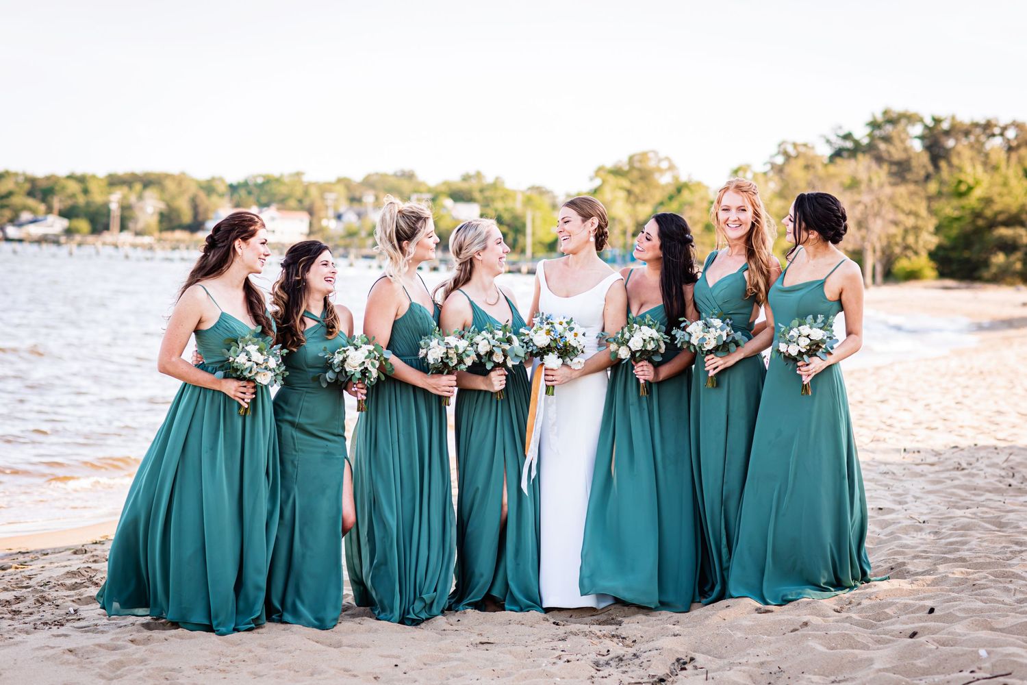Bridesmaids in matching teal gowns pose together on a sandy beach during sunset.