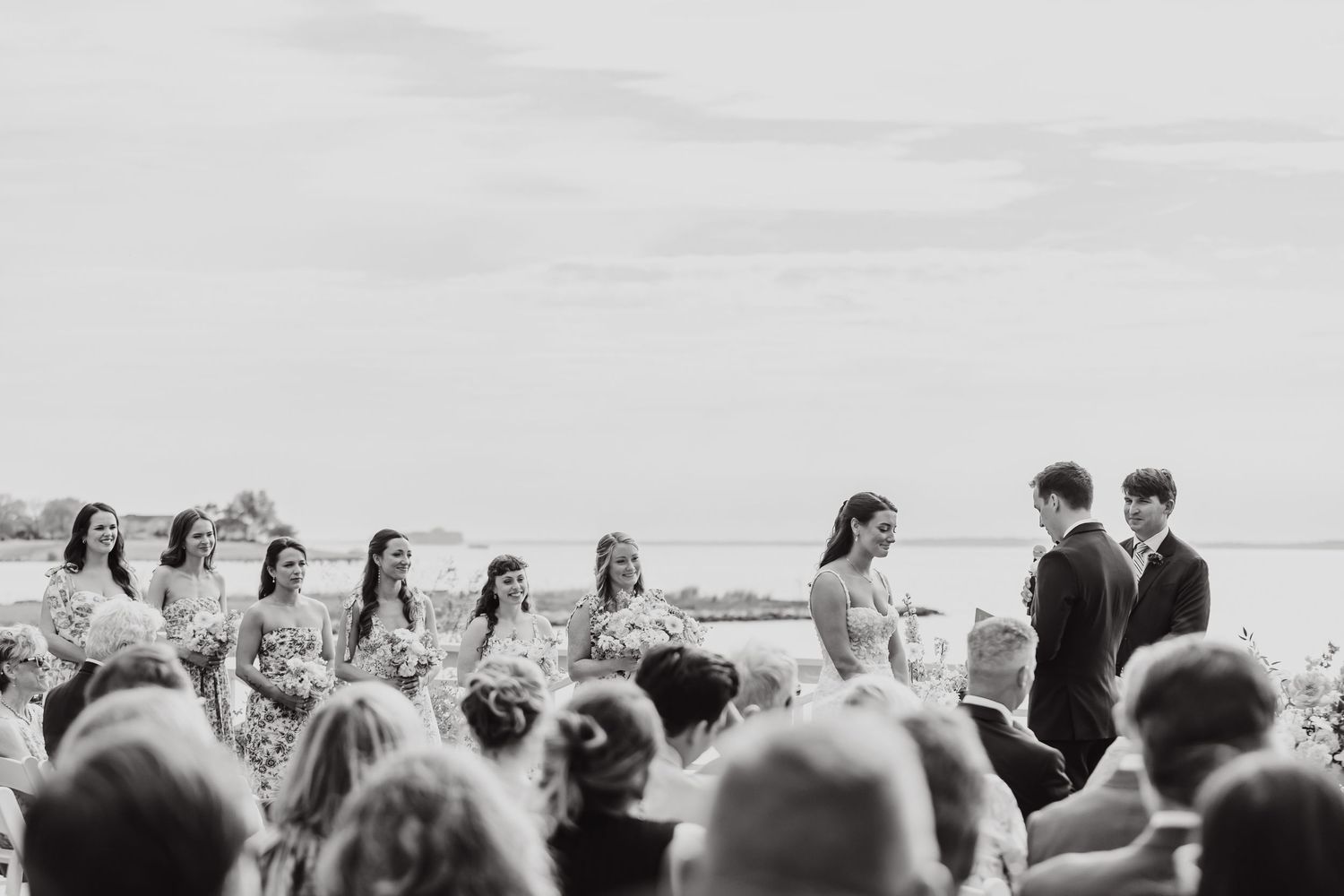 A black and white photo of a wedding ceremony taking place outdoors with guests seated.