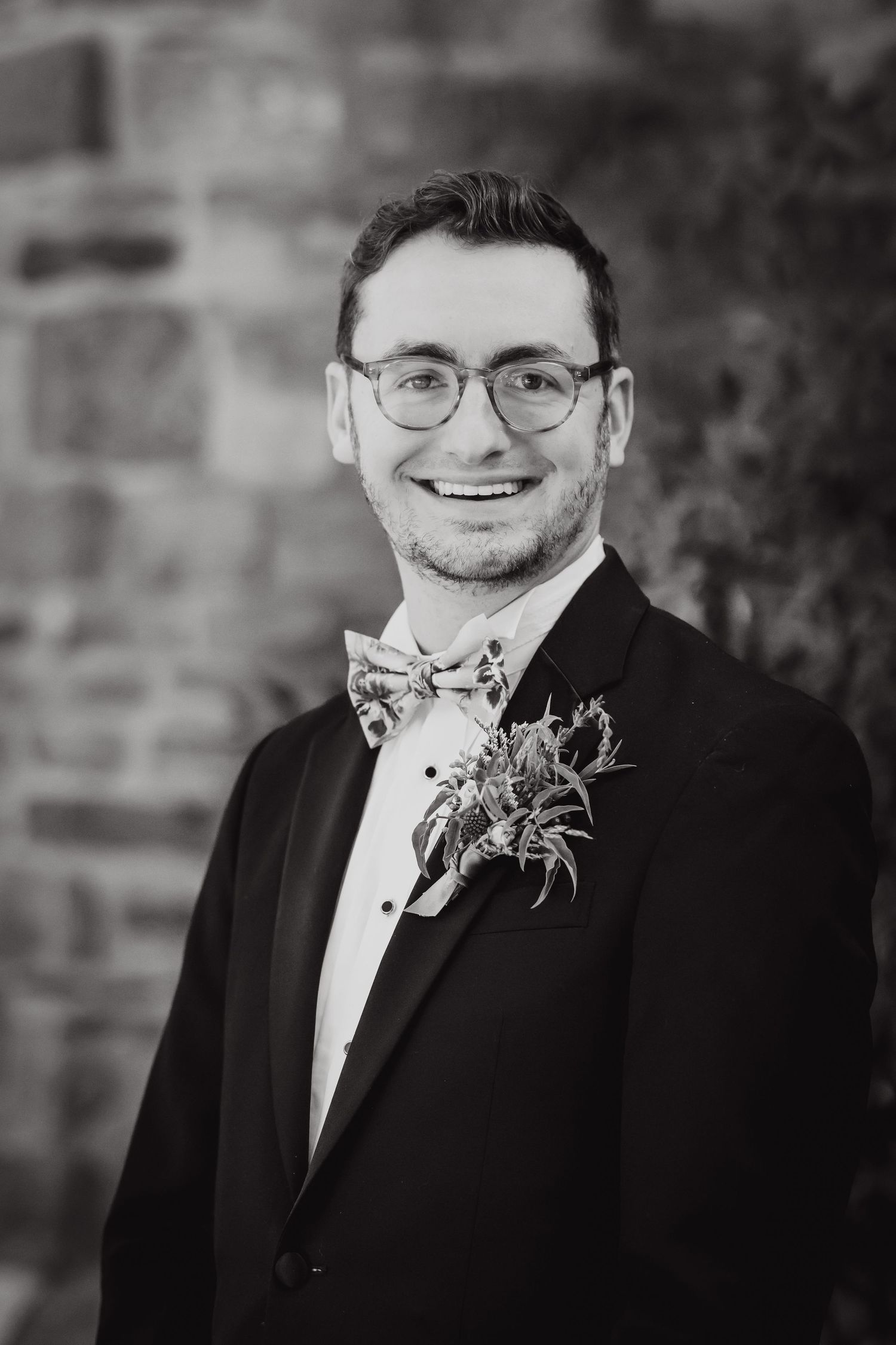 A formal black and white portrait showing a person in a bow tie and tuxedo with boutonniere.