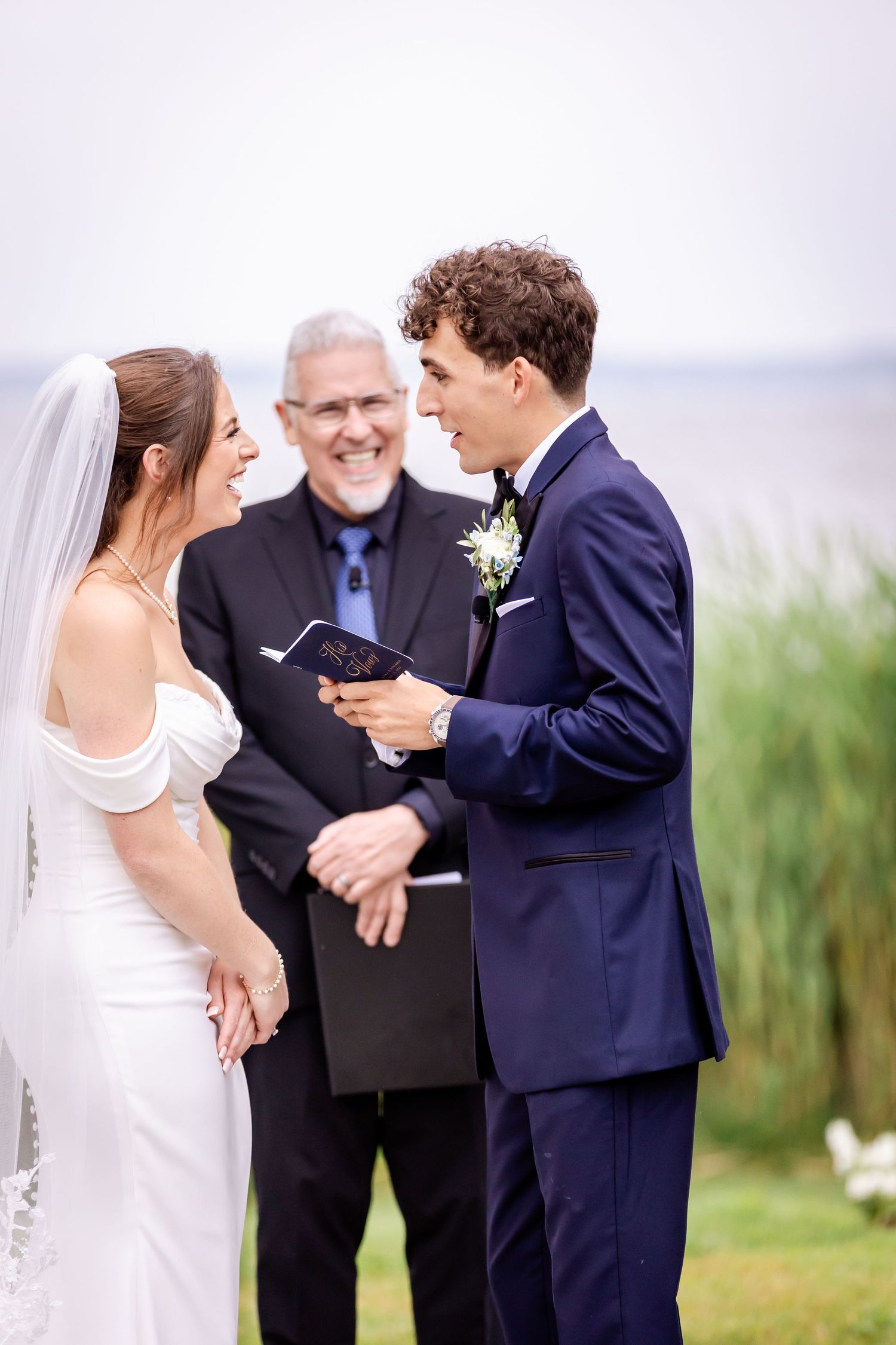 A wedding ceremony takes place outdoors with tall grass and natural scenery in the background.