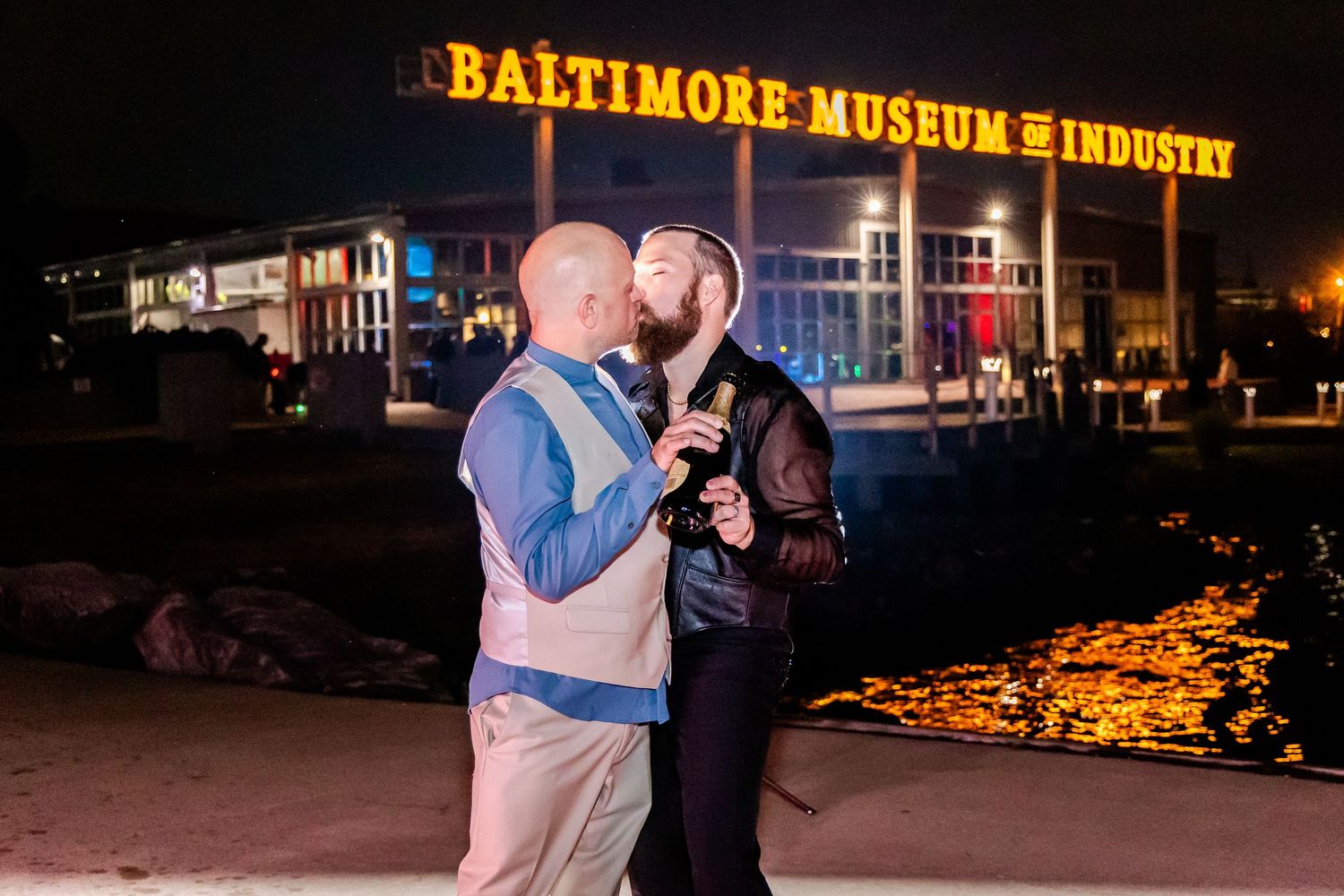 A couple dances together at night with the illuminated Baltimore Museum of Industry sign visible in the background.