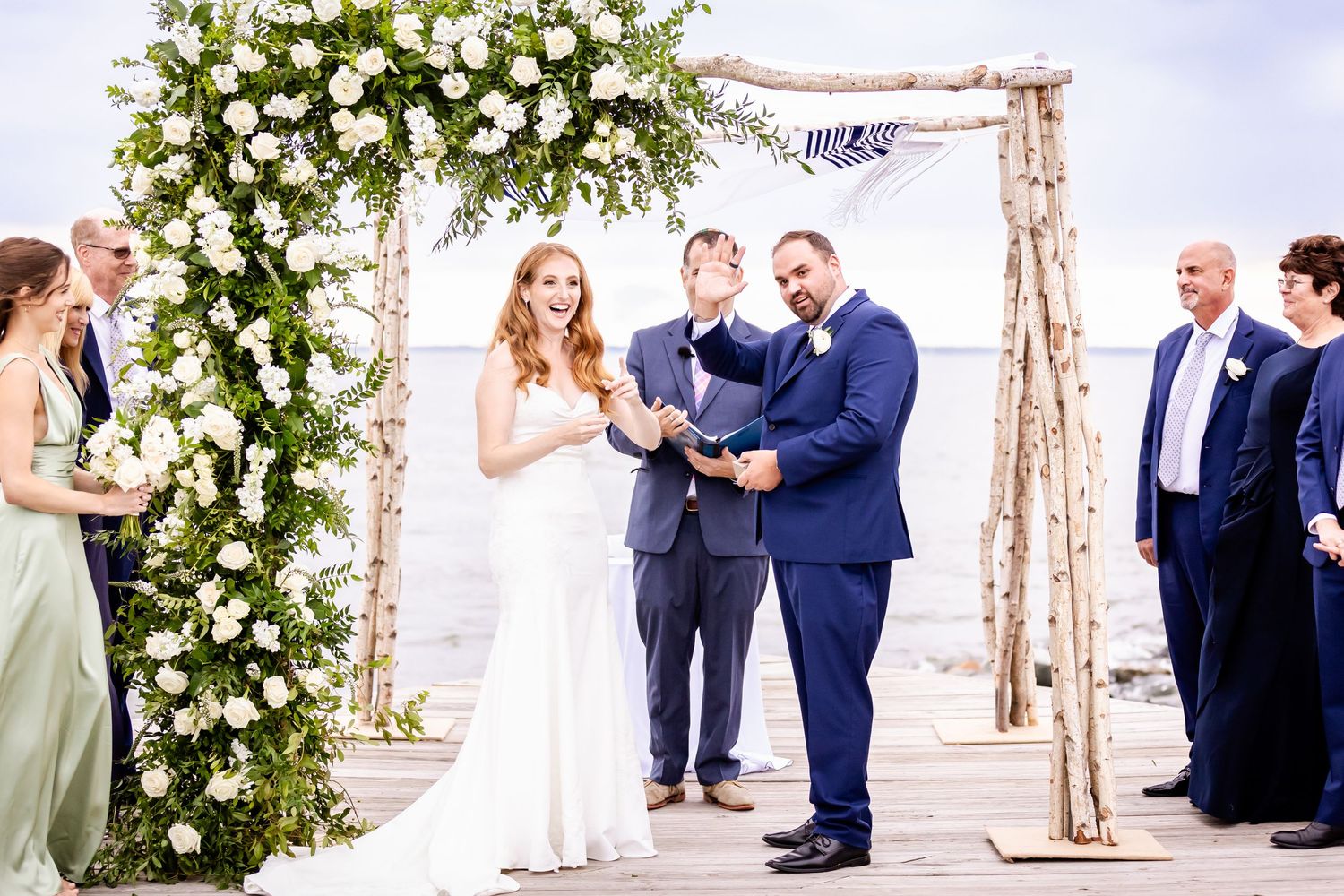 Rustic beach wedding ceremony under wooden arch decorated with white floral arrangements and greenery.