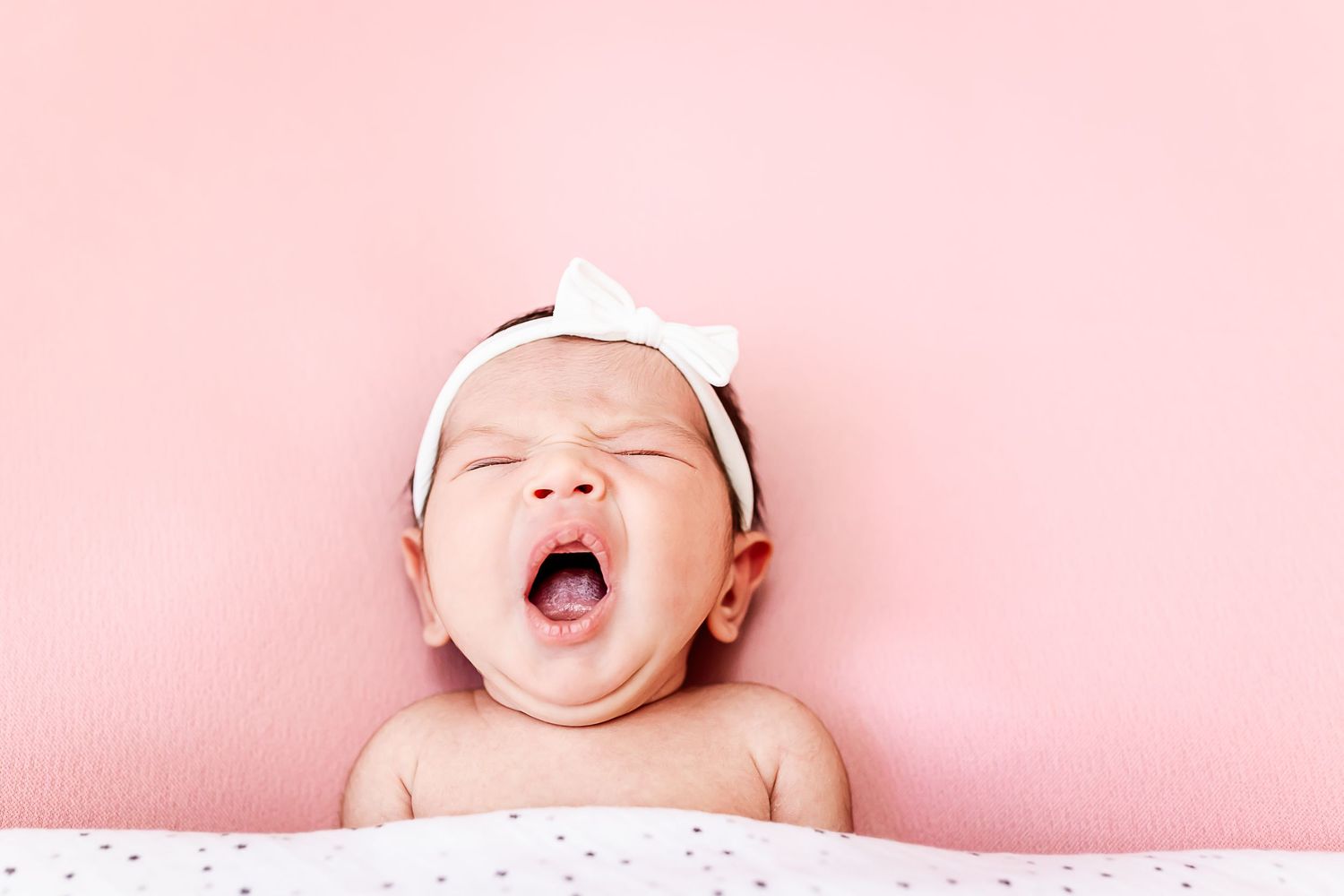 Baby yawning and making adorable expressions against a pink background.