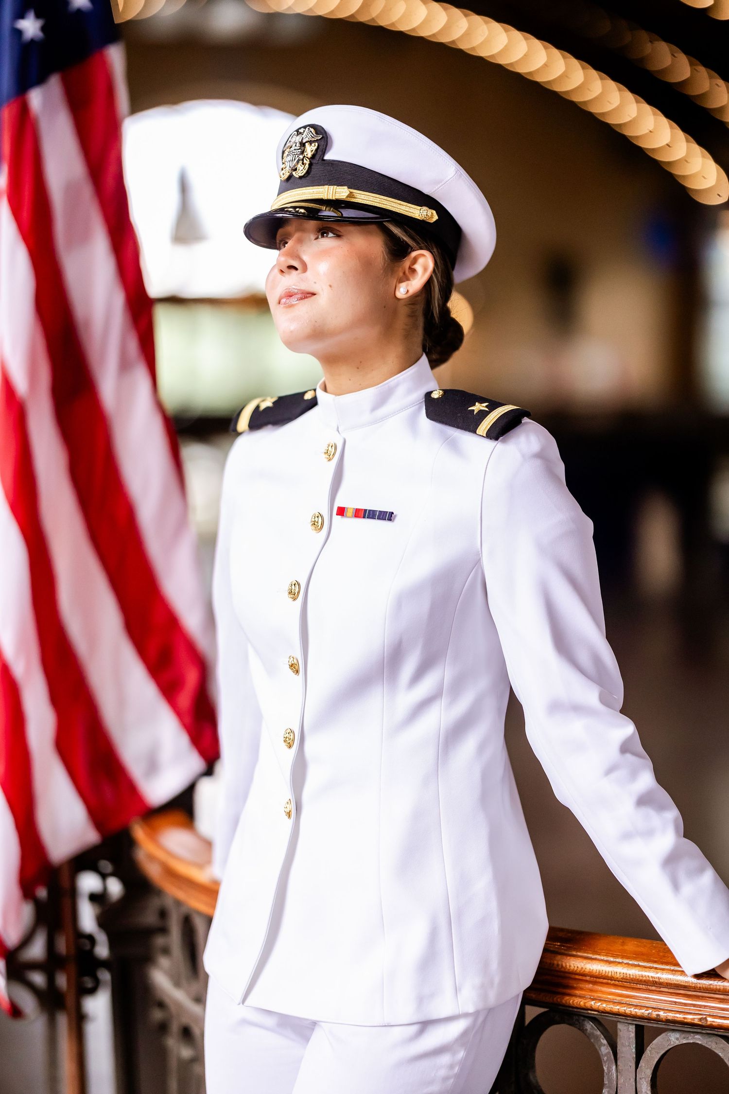 Military personnel in white dress uniforms standing at attention with American flags in background.