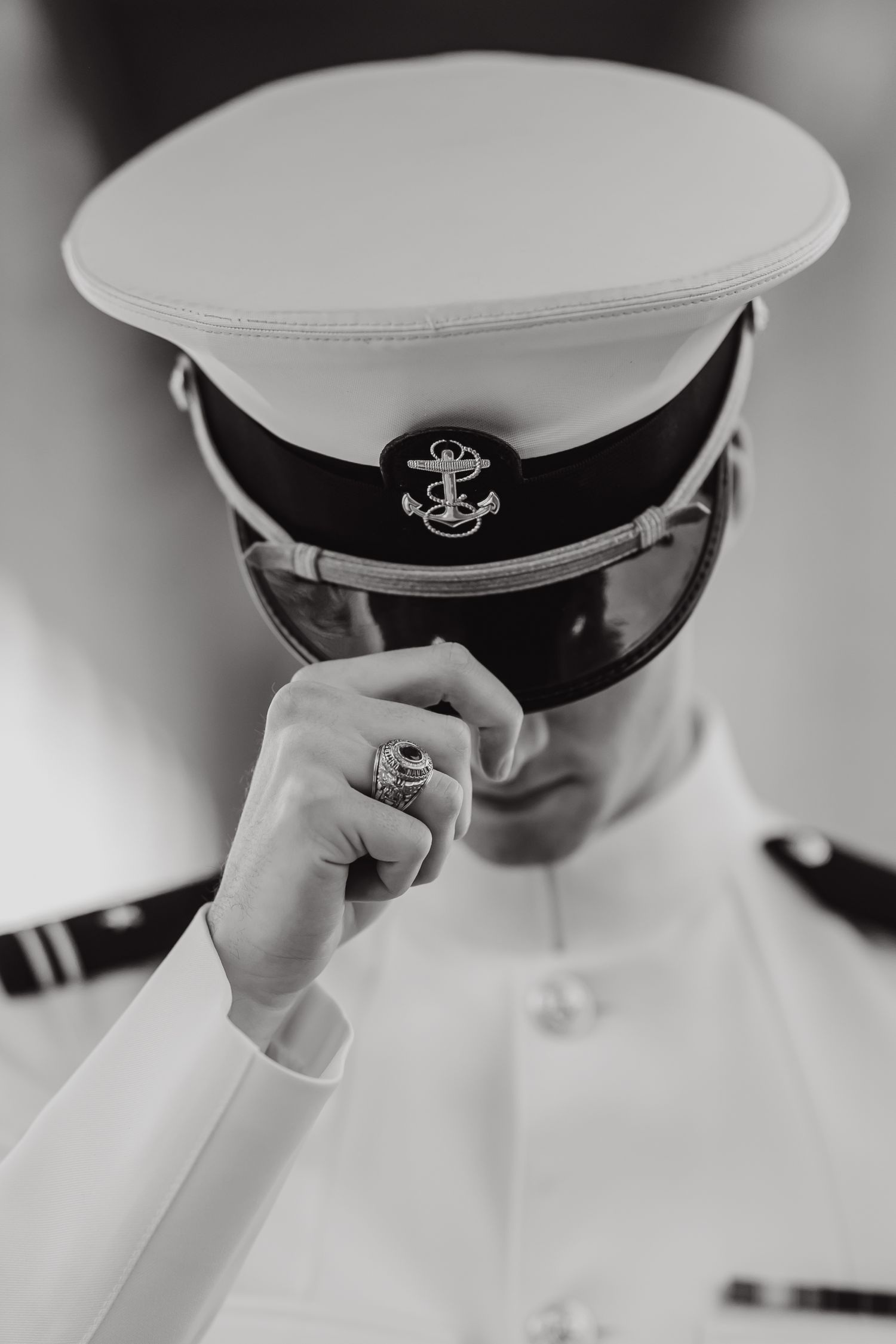 Black and white portrait of a naval officer in white dress uniform adjusting cap with anchor insignia.
